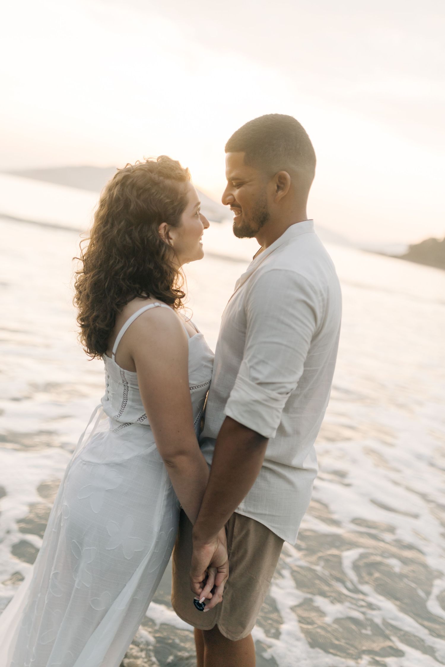 Intimate moment between couple on beach with gentle waves in background.