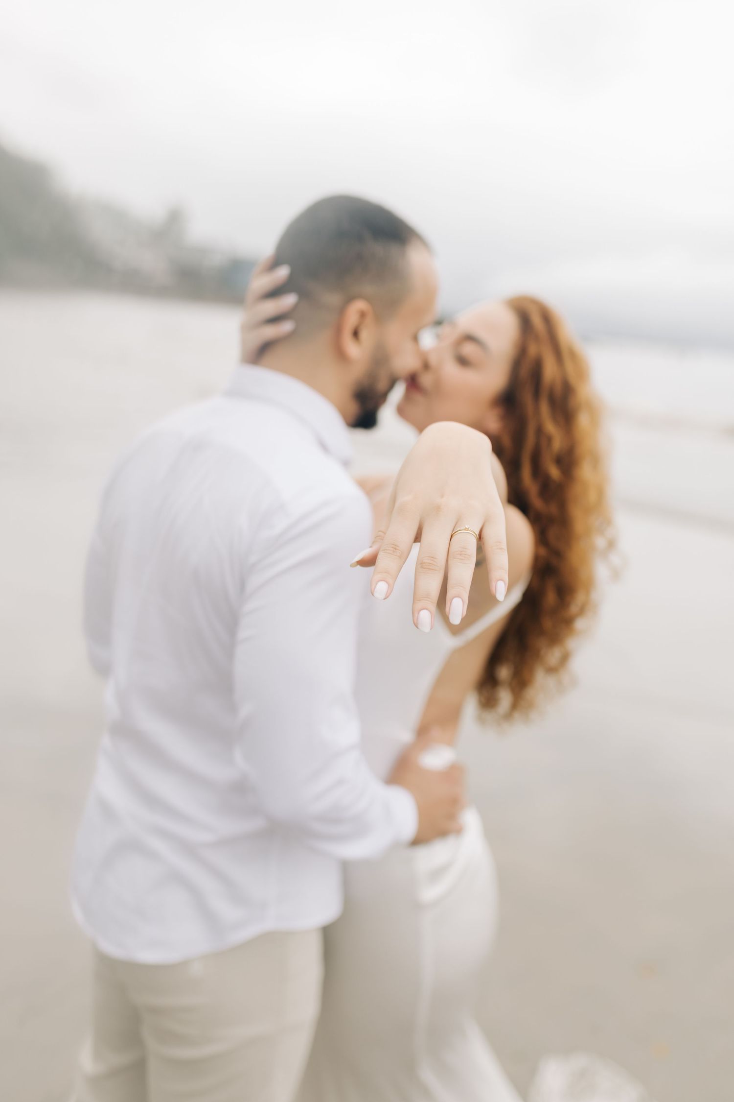 Dreamy beach engagement photos with couple in white and beige attire sharing romantic moments.