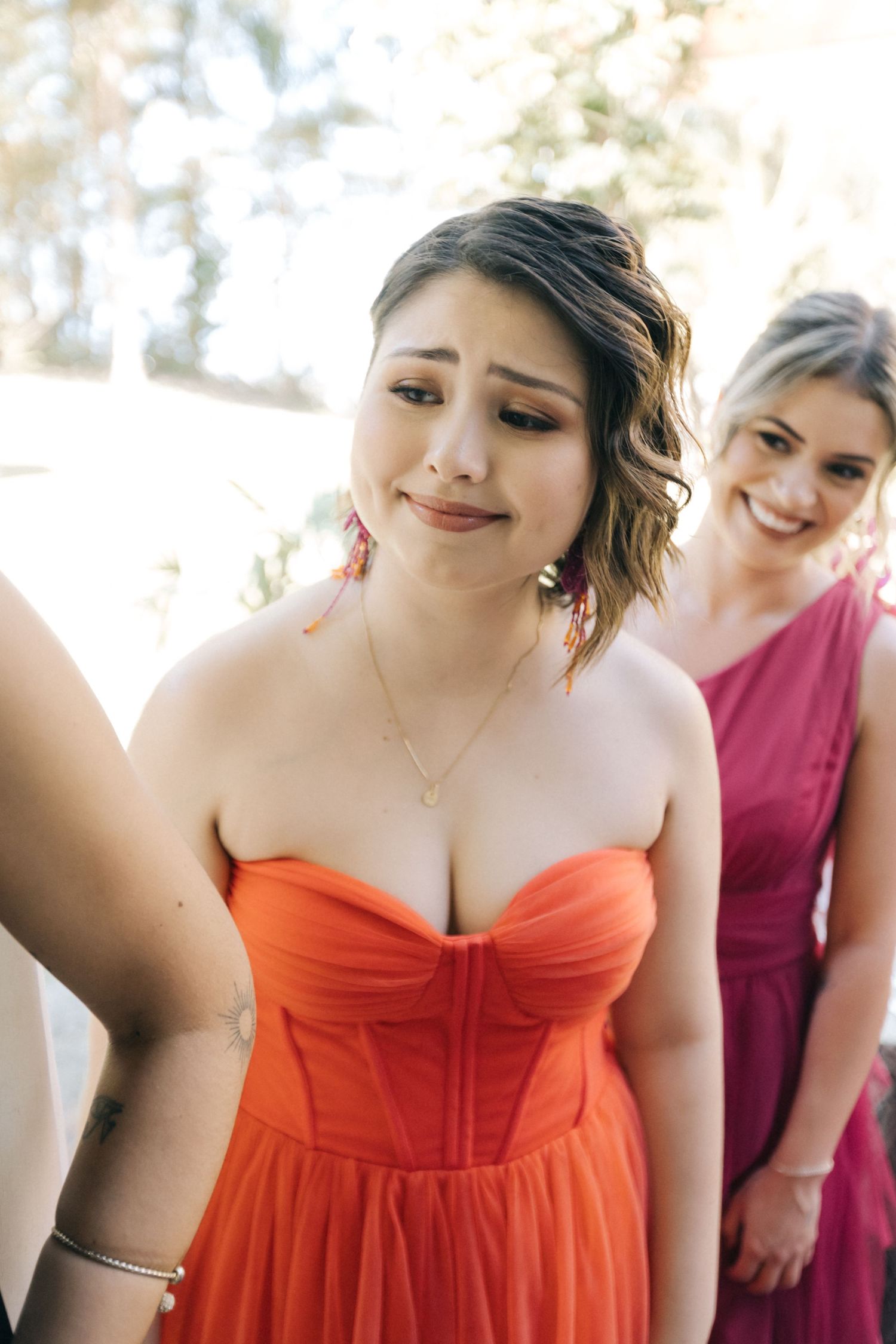 Group wearing coral and burgundy bridesmaid dresses share candid moments during wedding preparations.