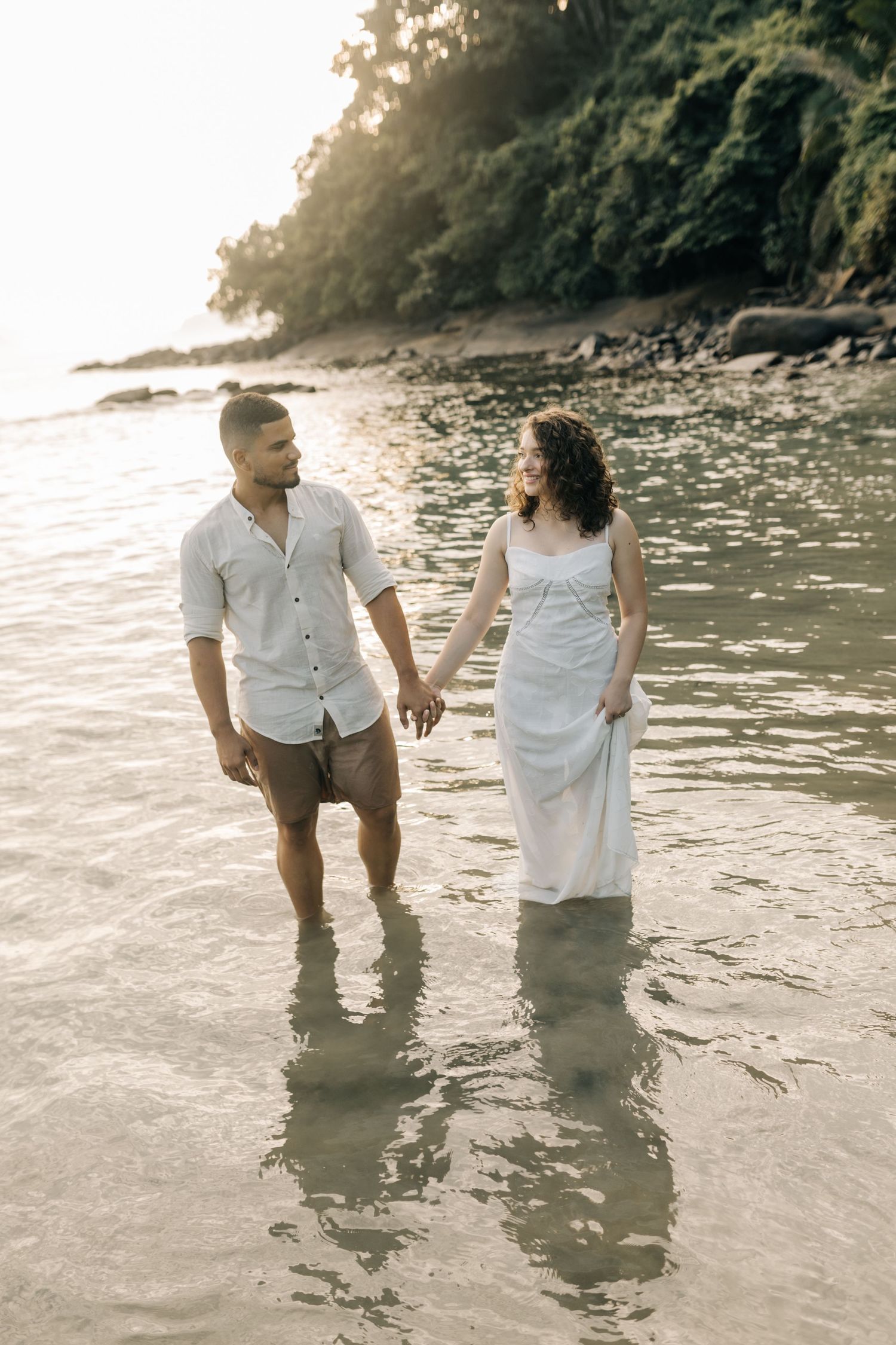 Couple wading together in shallow ocean water during a beach photoshoot.
