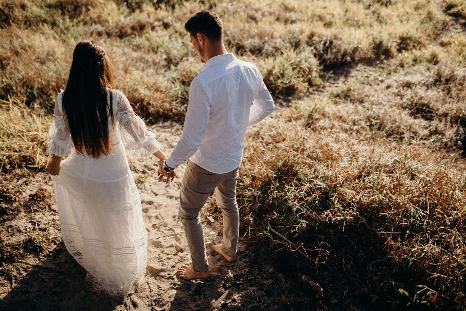 Couple walking through golden grass during sunset wedding photoshoot.