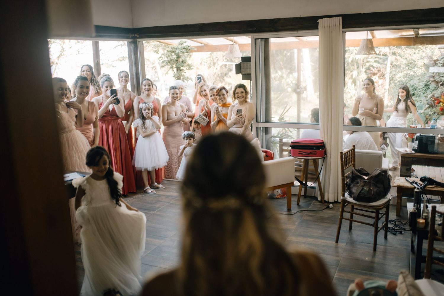 Bridesmaids in coral dresses watching first look moment at indoor wedding venue.