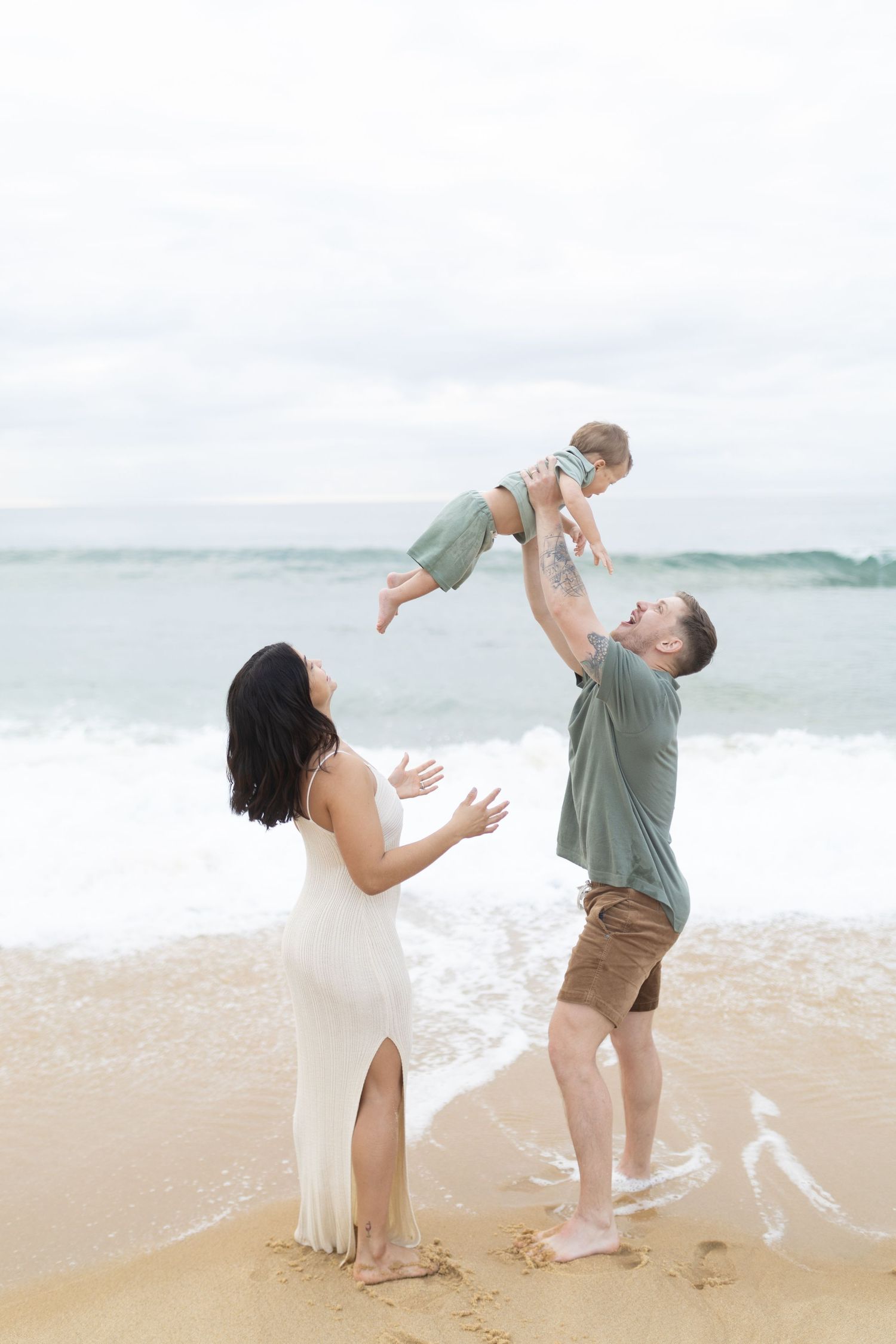 A family plays and laughs together on a sandy beach near the ocean.