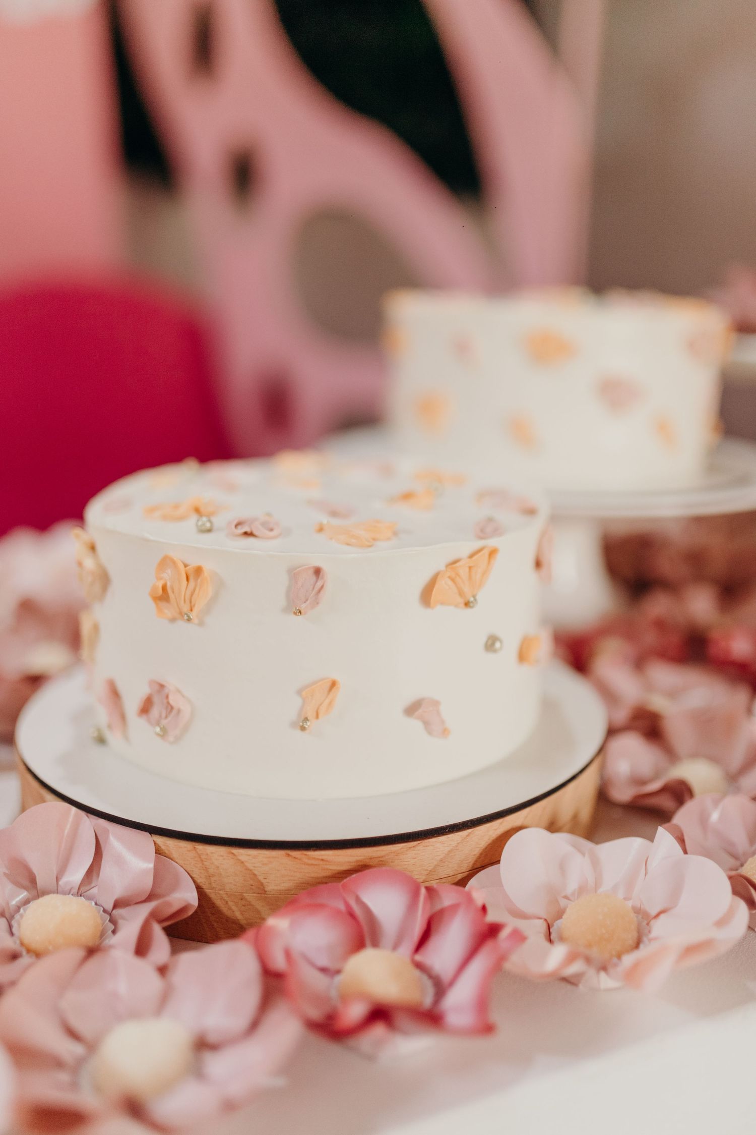 White cake with delicate pink and peach decorations surrounded by flower petals.