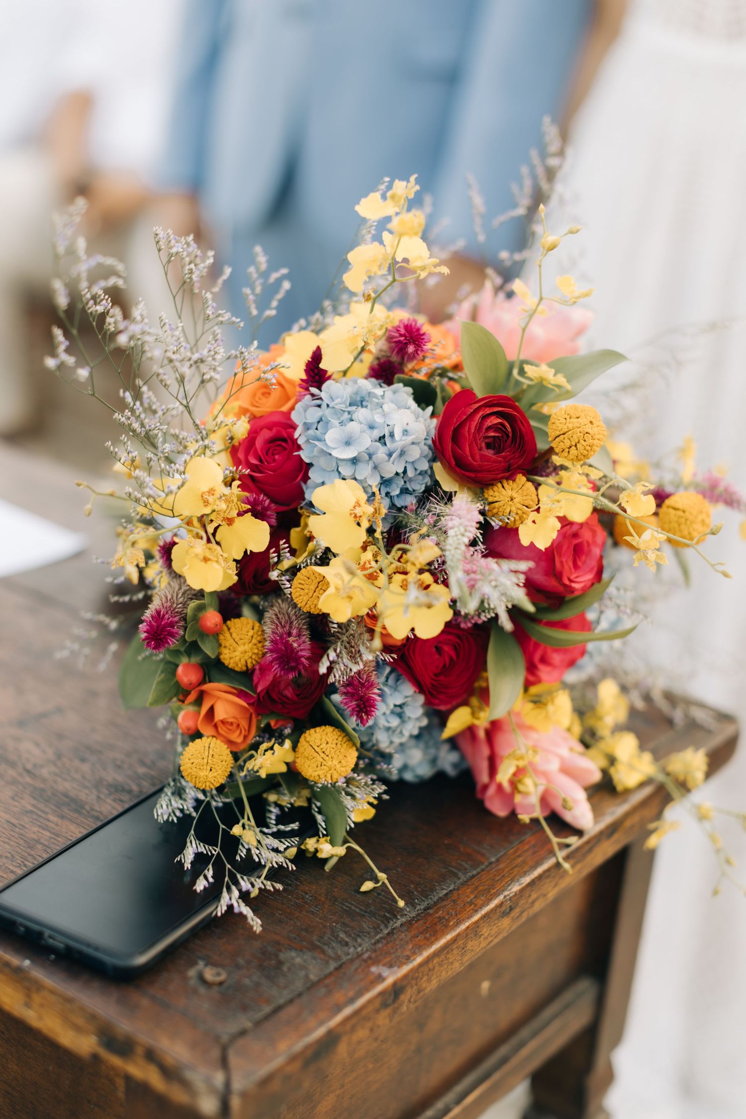Colorful wedding floral arrangement with yellow, red and blue flowers on wooden table.