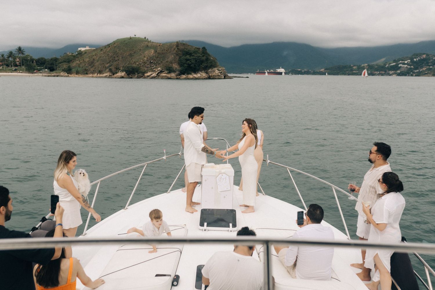 A group celebrates on a boat deck with mountains and water in the background.
