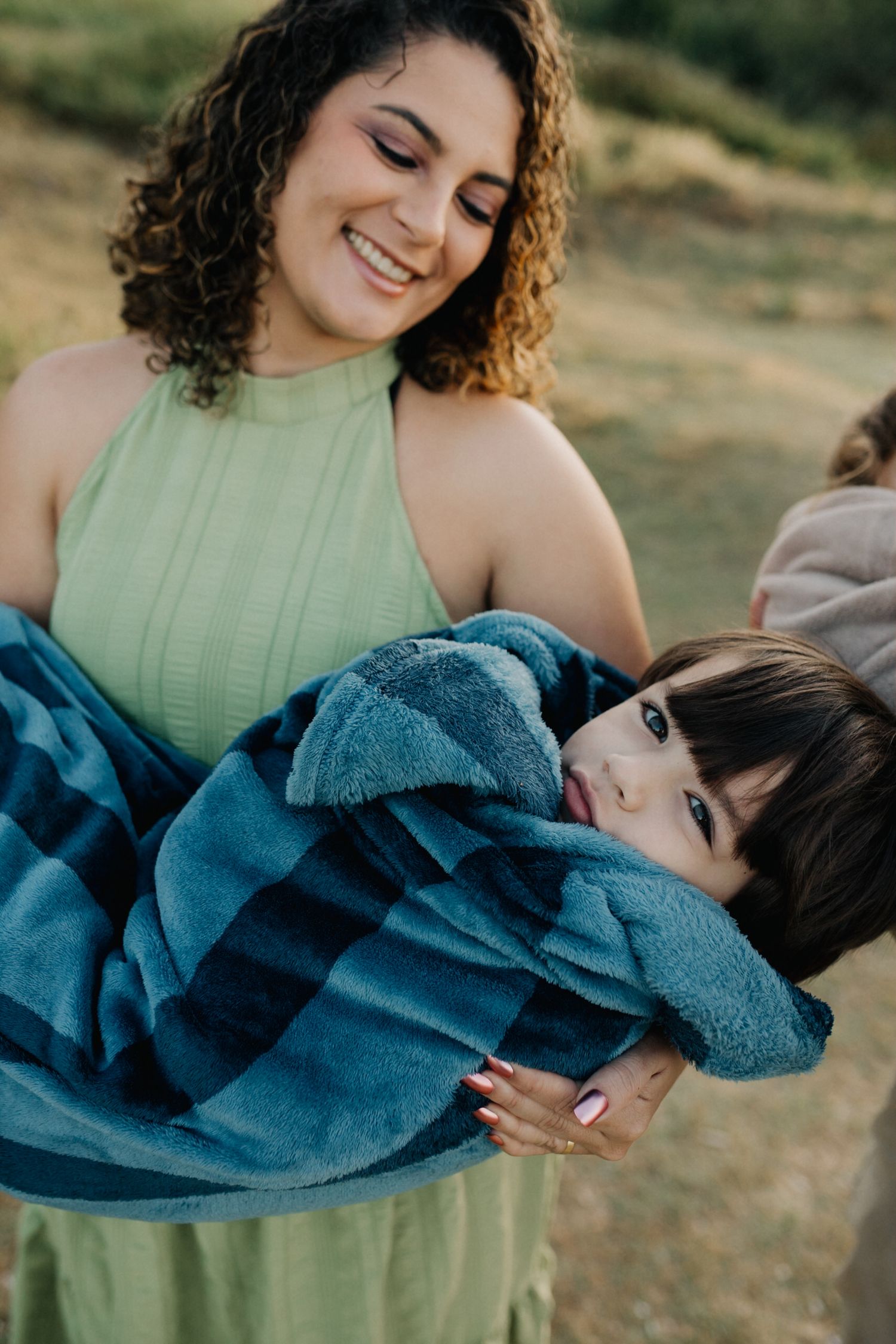 Woman in mint green dress shares tender moment with child wrapped in blue blanket.