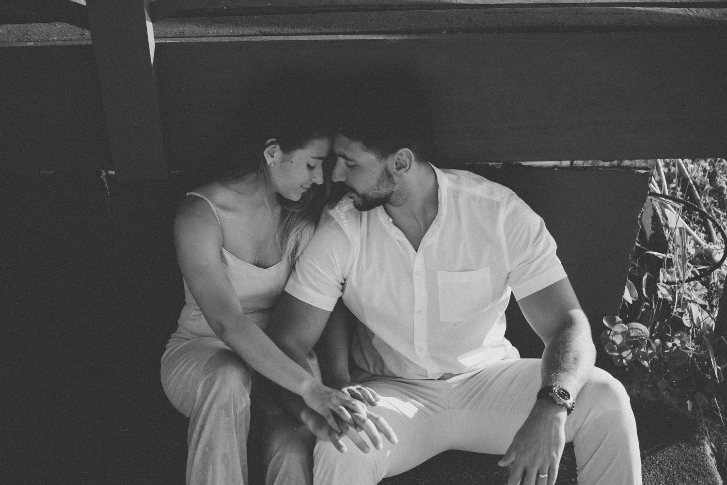 Black and white portrait of couple sharing intimate moment on rustic bench.