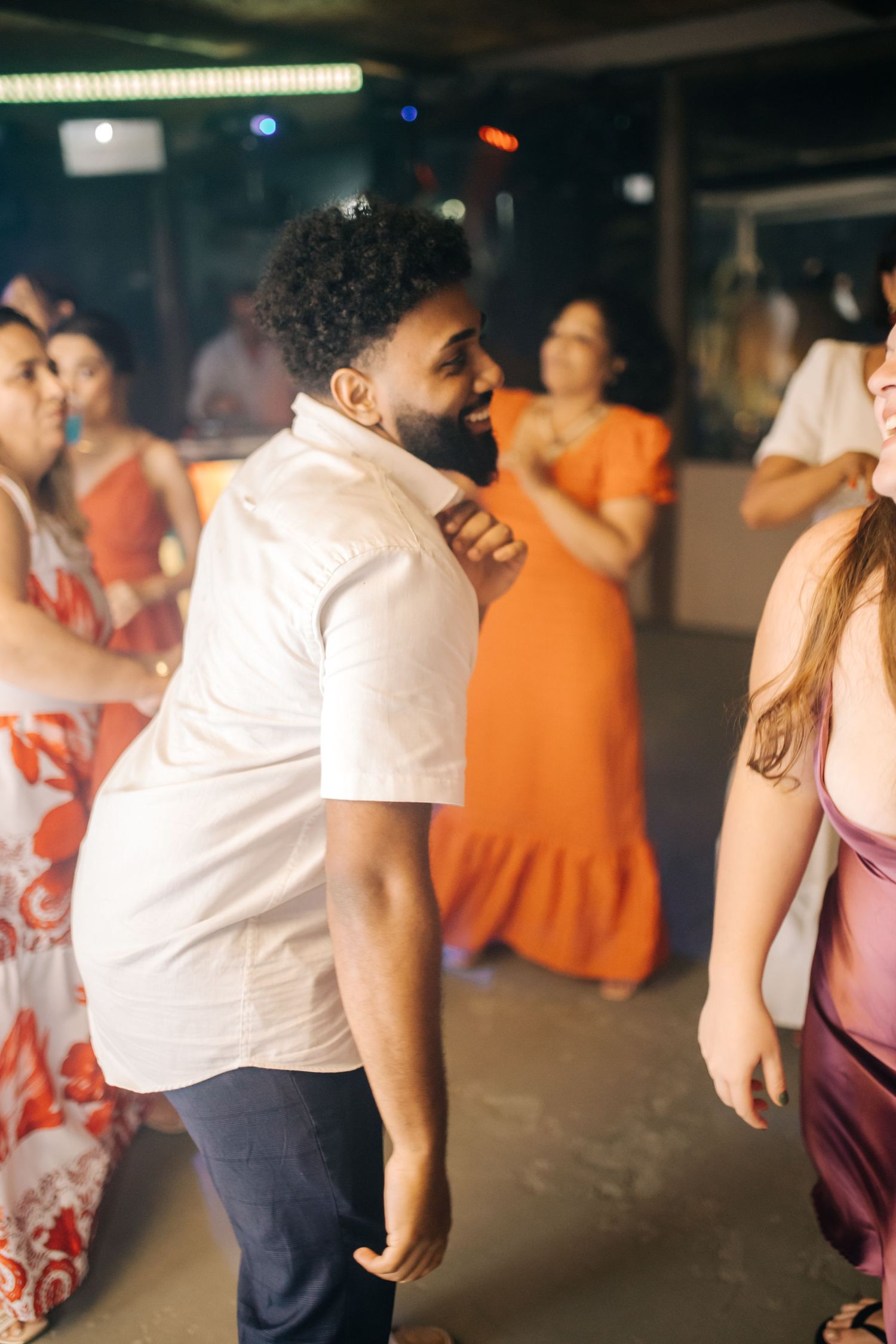Wedding reception guests dancing energetically on the dance floor in orange and white attire.