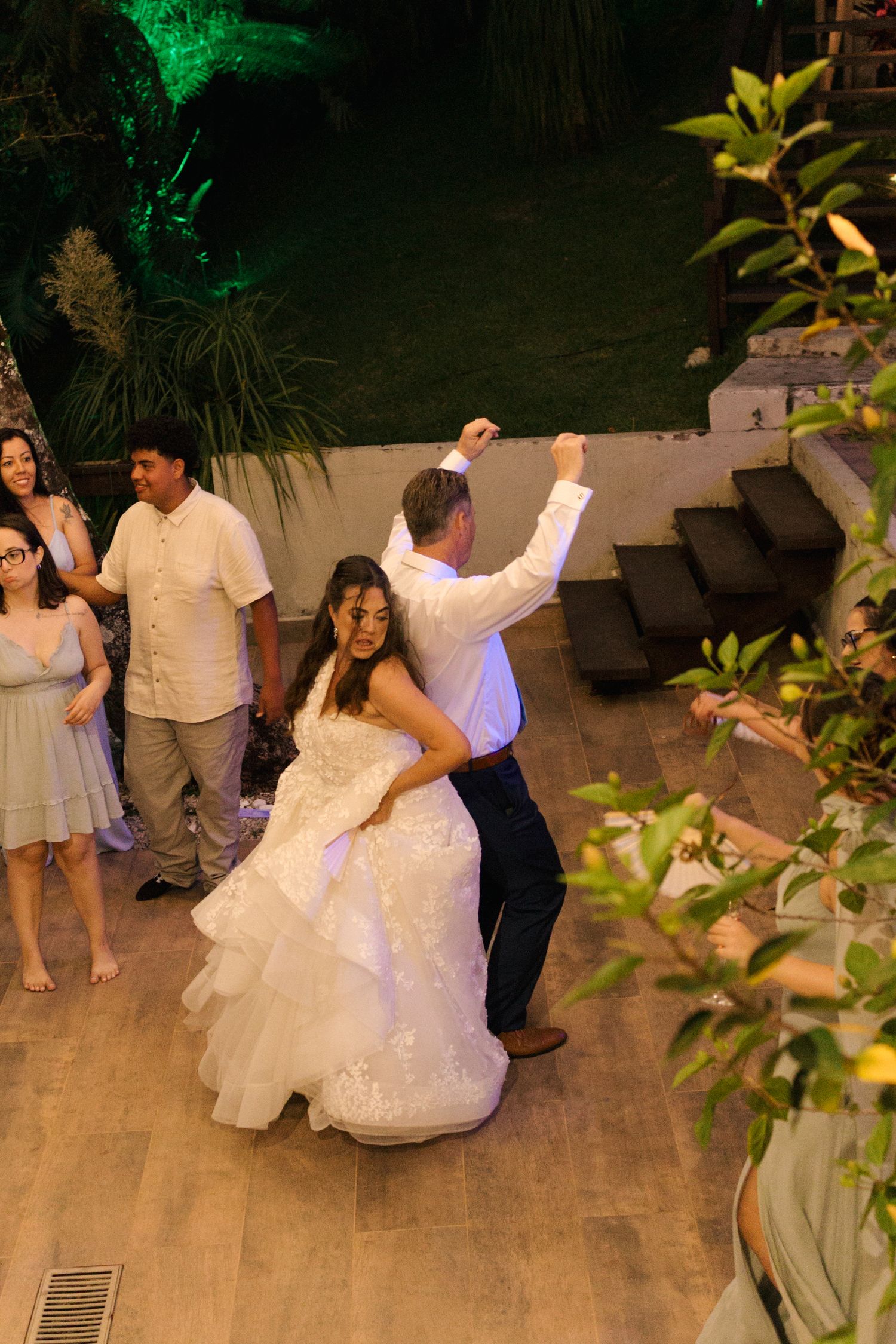 Wedding reception dancing captured at night with green uplighting and tropical garden surroundings.