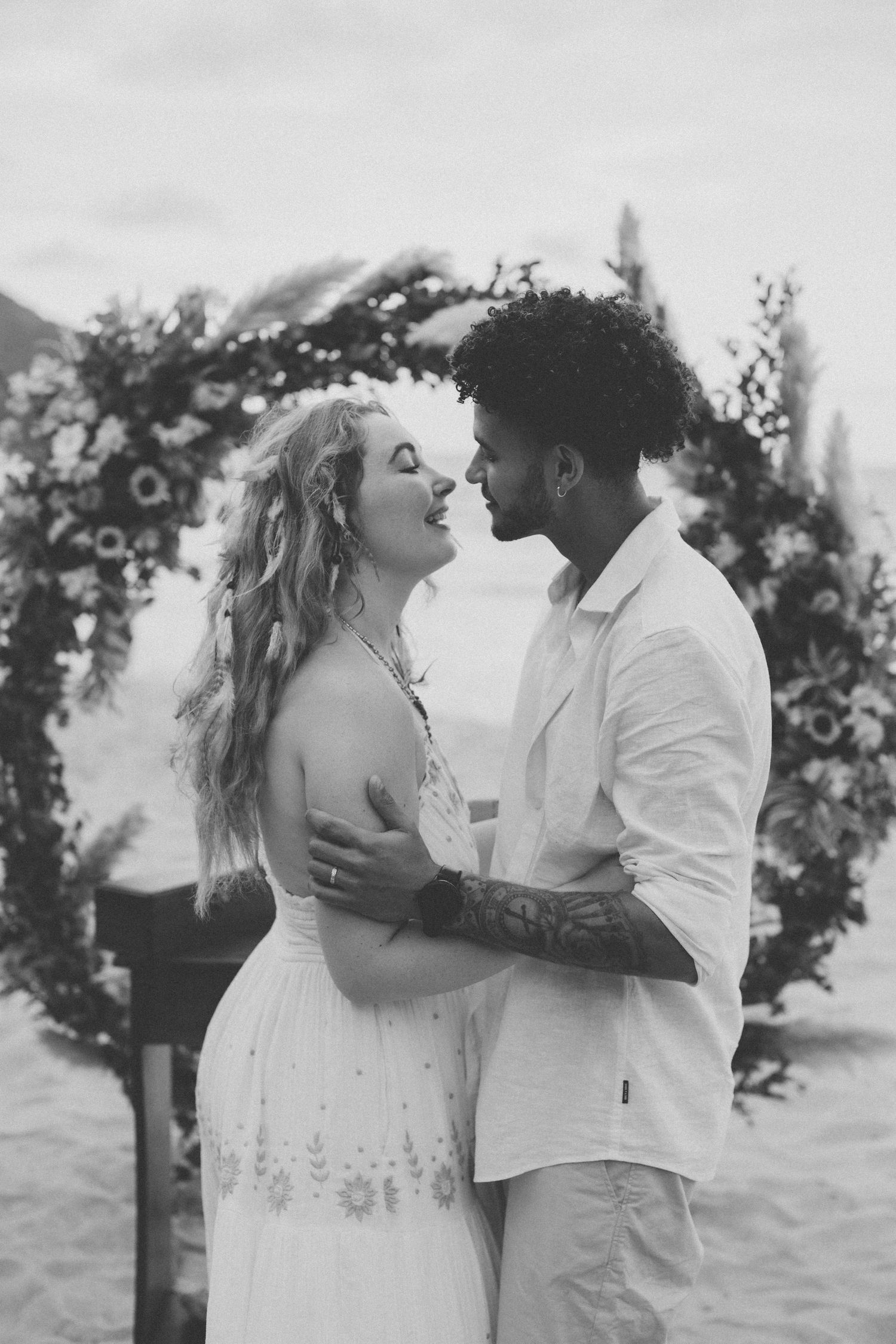 Black and white photo of a couple sharing an intimate moment under a floral wedding arch.
