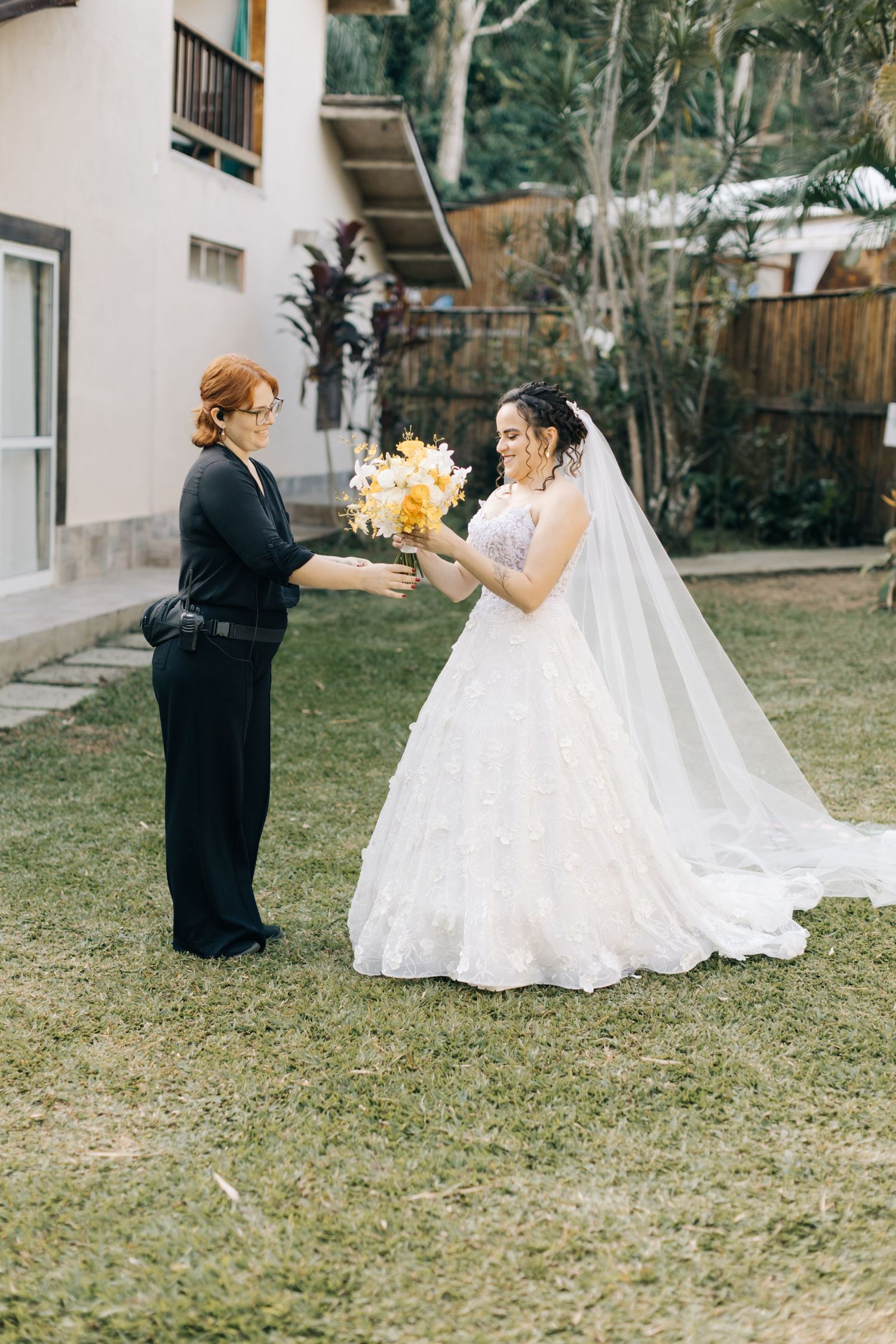 A wedding moment outdoors where two people exchange a bouquet of yellow flowers.