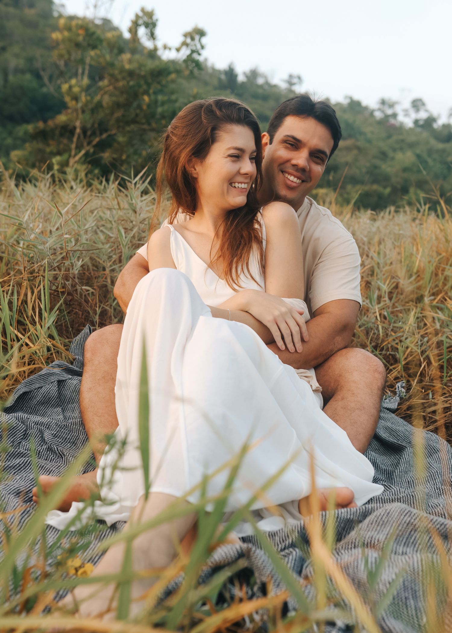 Couple laughing together while relaxing on blanket in grassy field.
