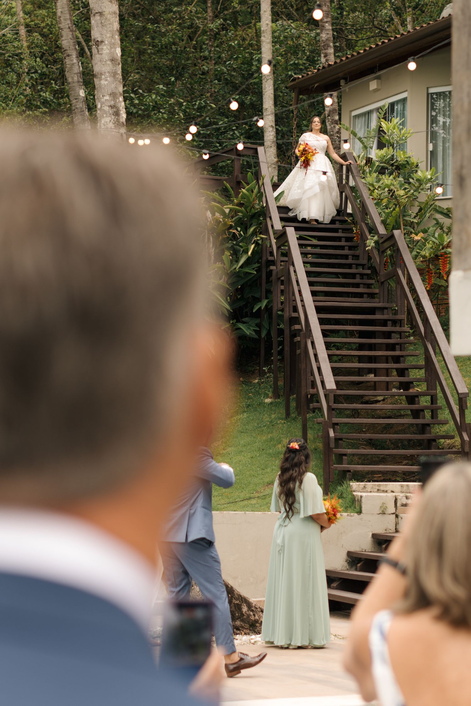 Wedding ceremony setup on outdoor wooden stairs decorated with string lights and greenery.