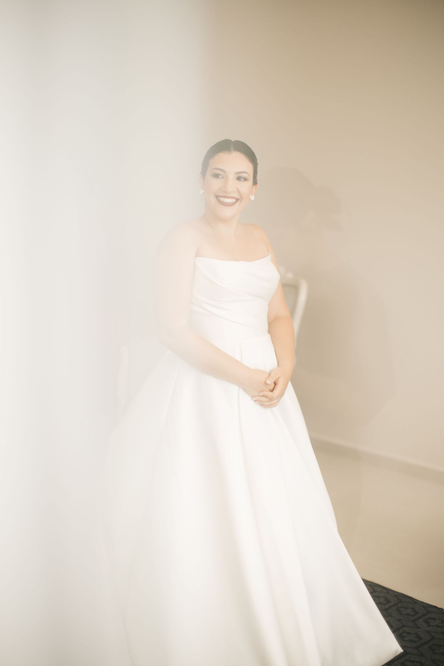 Soft dreamy bridal portrait in white wedding gown against neutral wall.