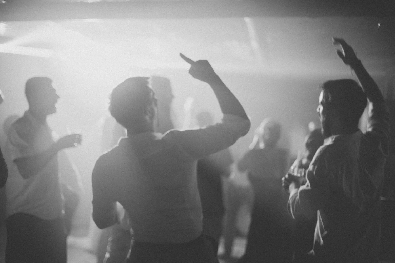 Dancing crowd silhouettes in a misty nightclub atmosphere with bright lights.