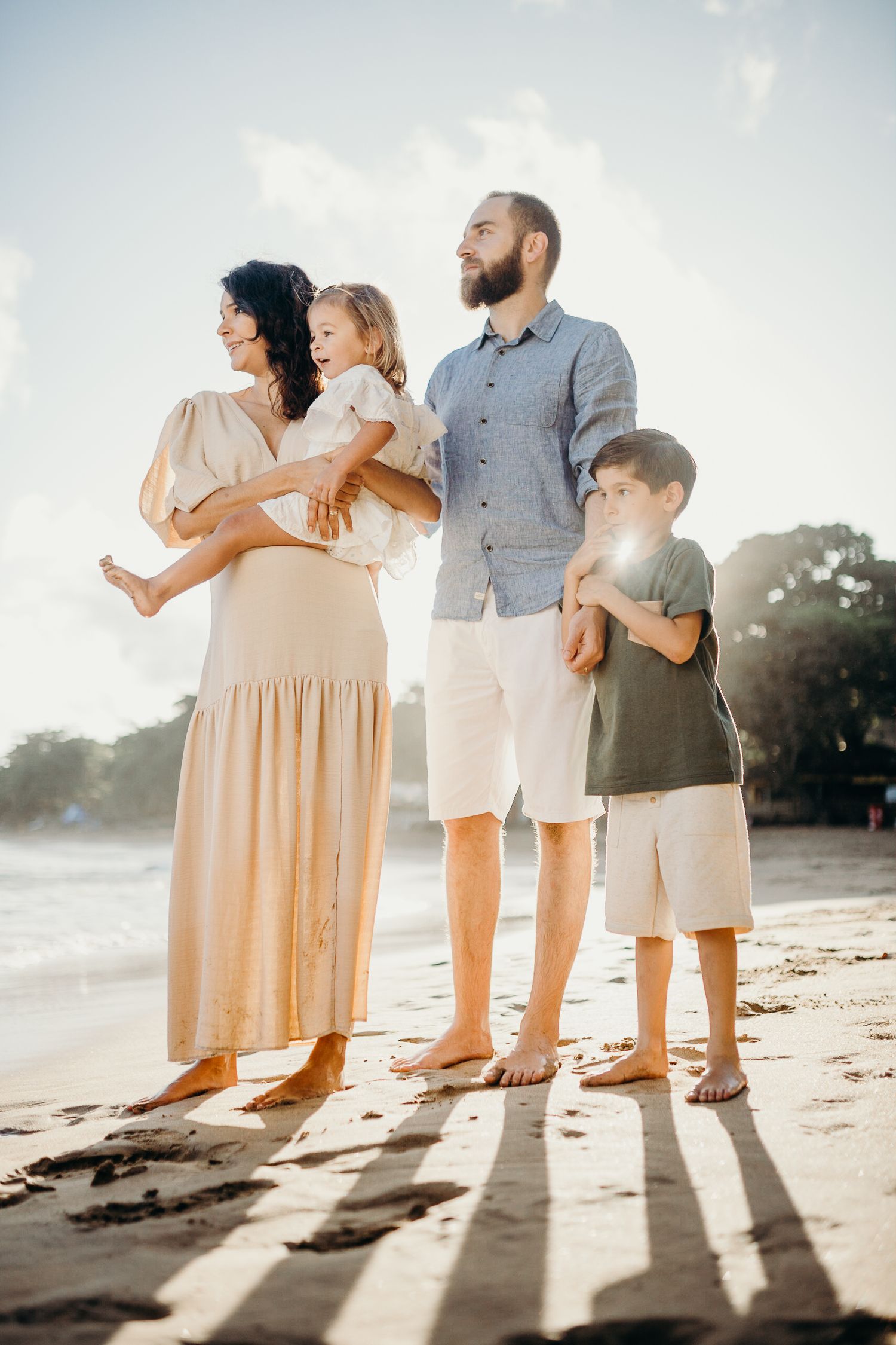 A family poses together on a beach during golden hour with dramatic shadows.