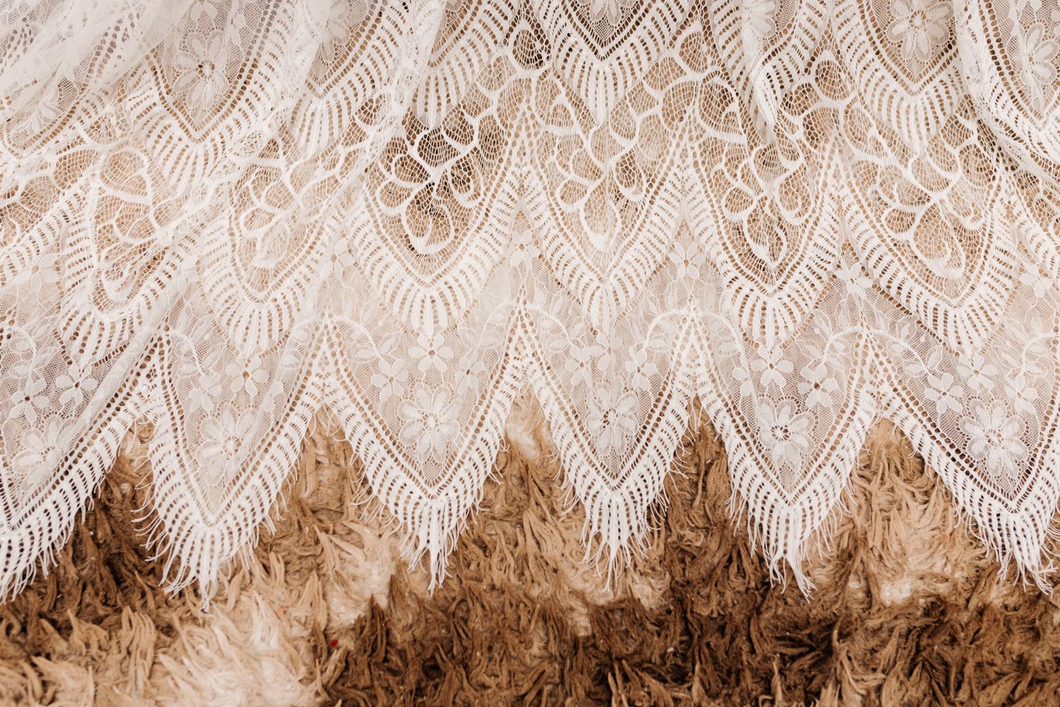 Close-up detail of intricate lace pattern from wedding dress with scalloped edges.