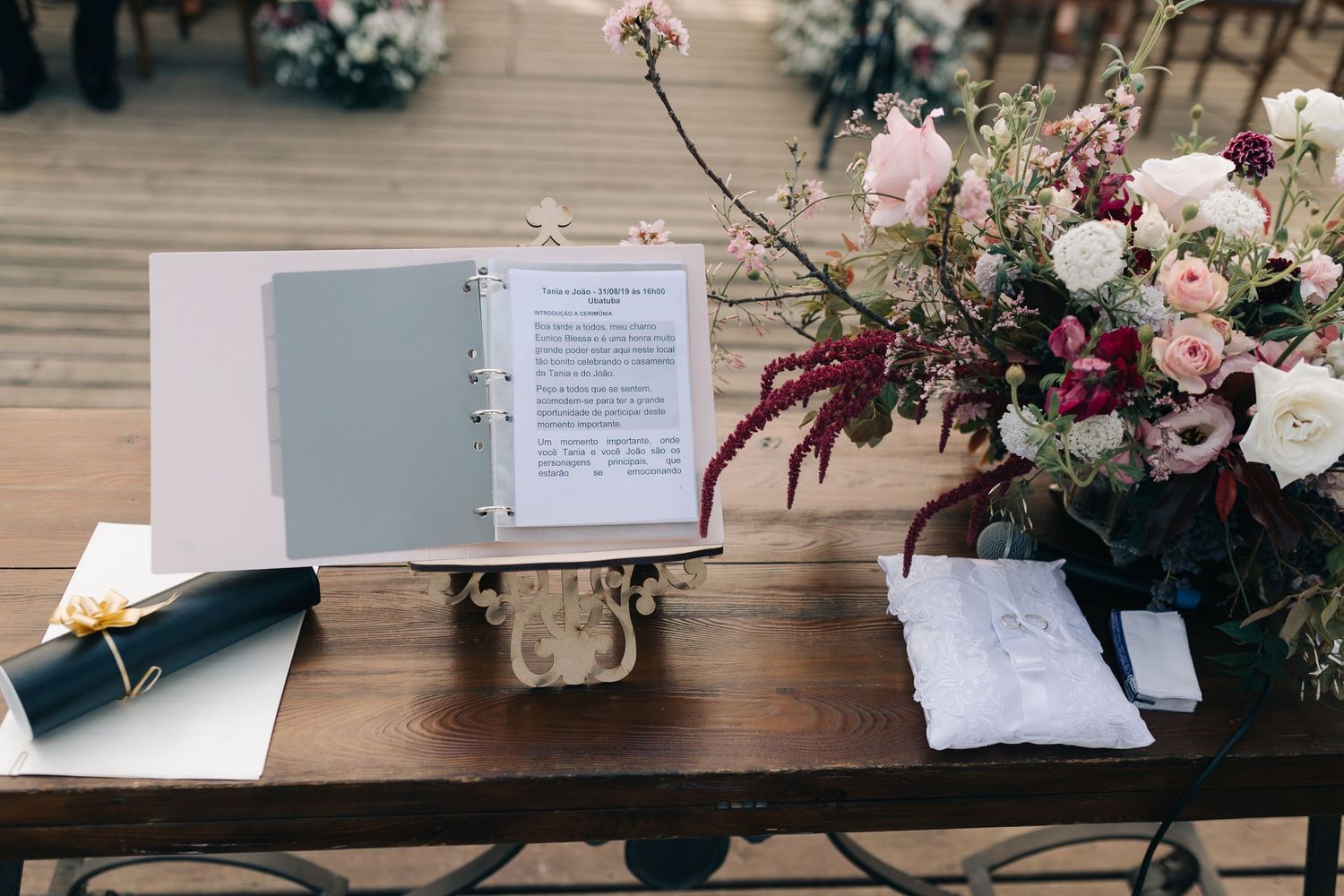 Wedding ceremony details with open book, floral arrangement and pen on rustic wooden table.