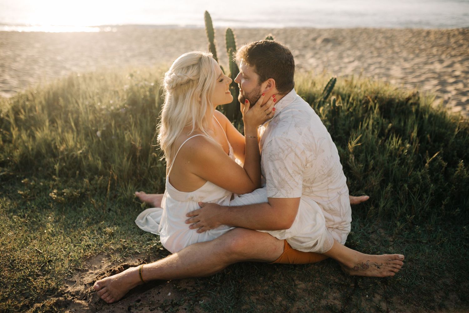 An intimate moment between a couple sitting on a grassy hillside during golden hour.