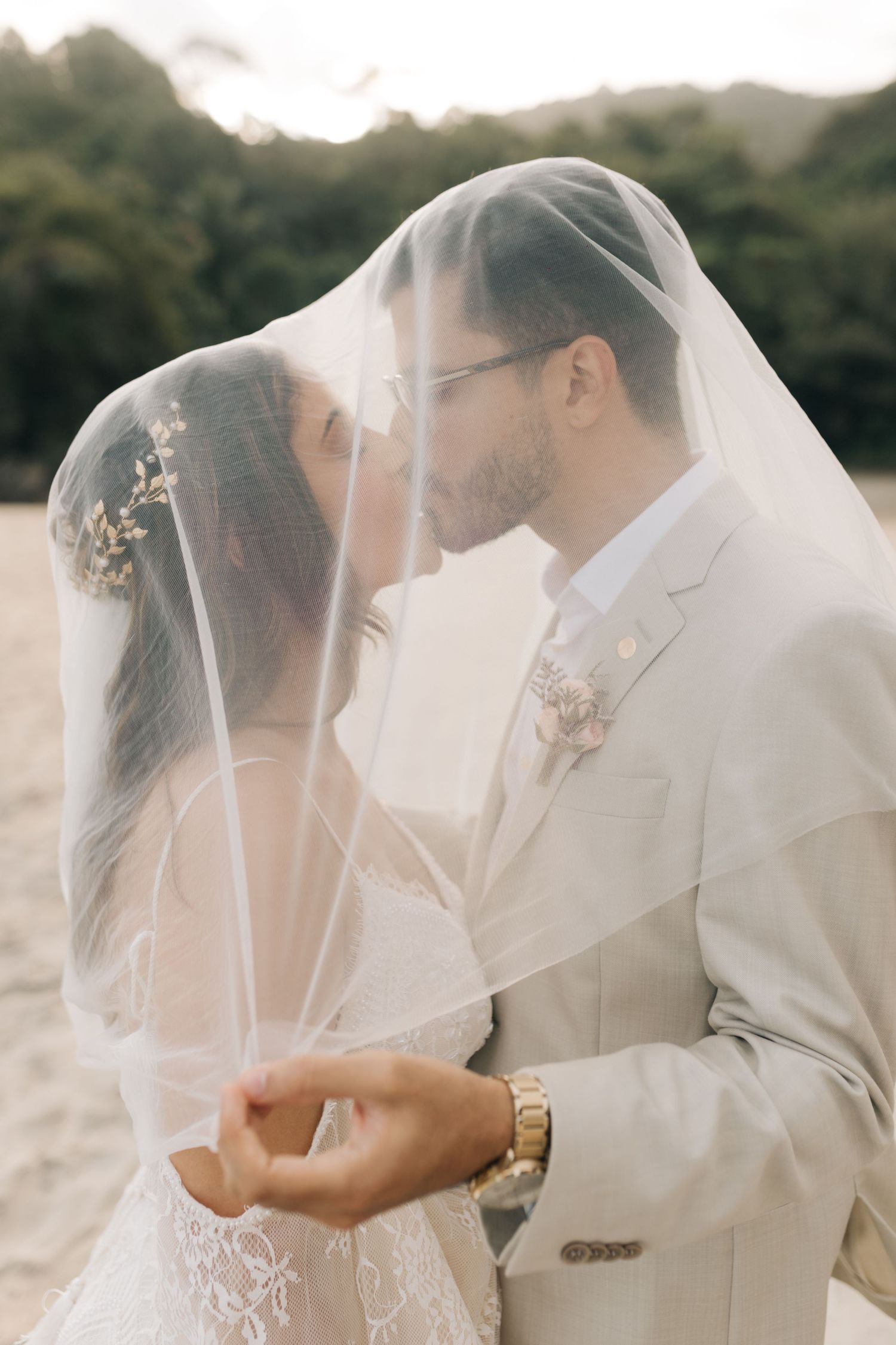 Romantic wedding portrait featuring a tender moment between newlyweds under a sheer veil at sunset.