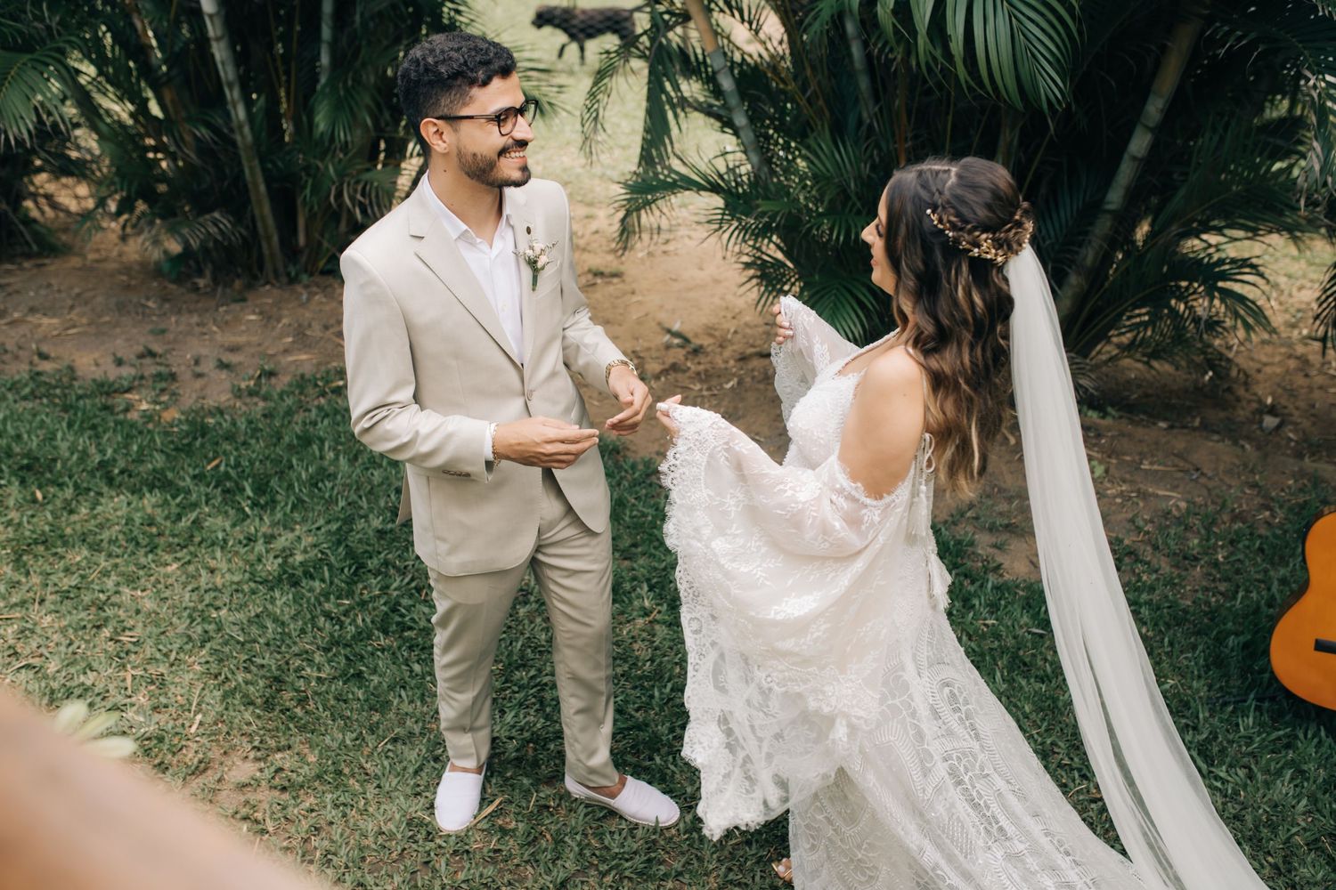 A newlywed couple shares a romantic moment in a tropical garden setting with palm trees and a guitar.