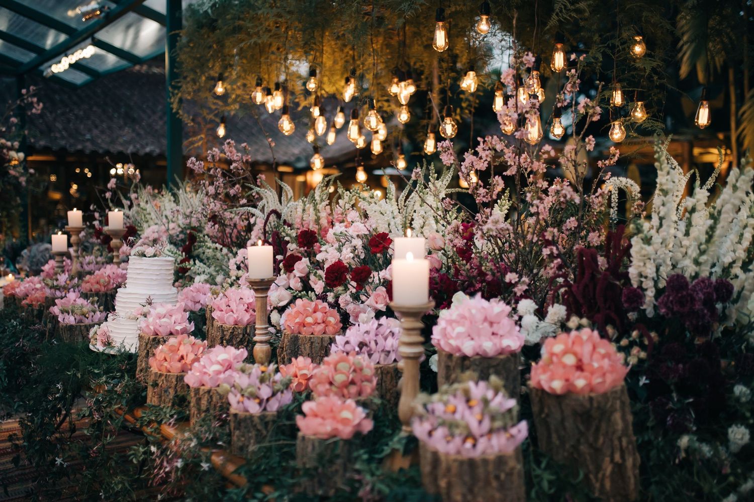 Evening wedding reception decorated with pink floral arrangements and hanging lights.