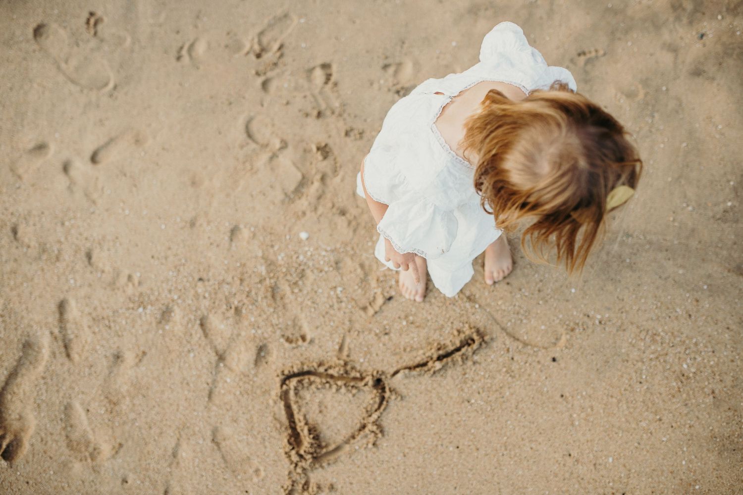 A heart shape drawn in sand with a figure in a white dress looking down from above.
