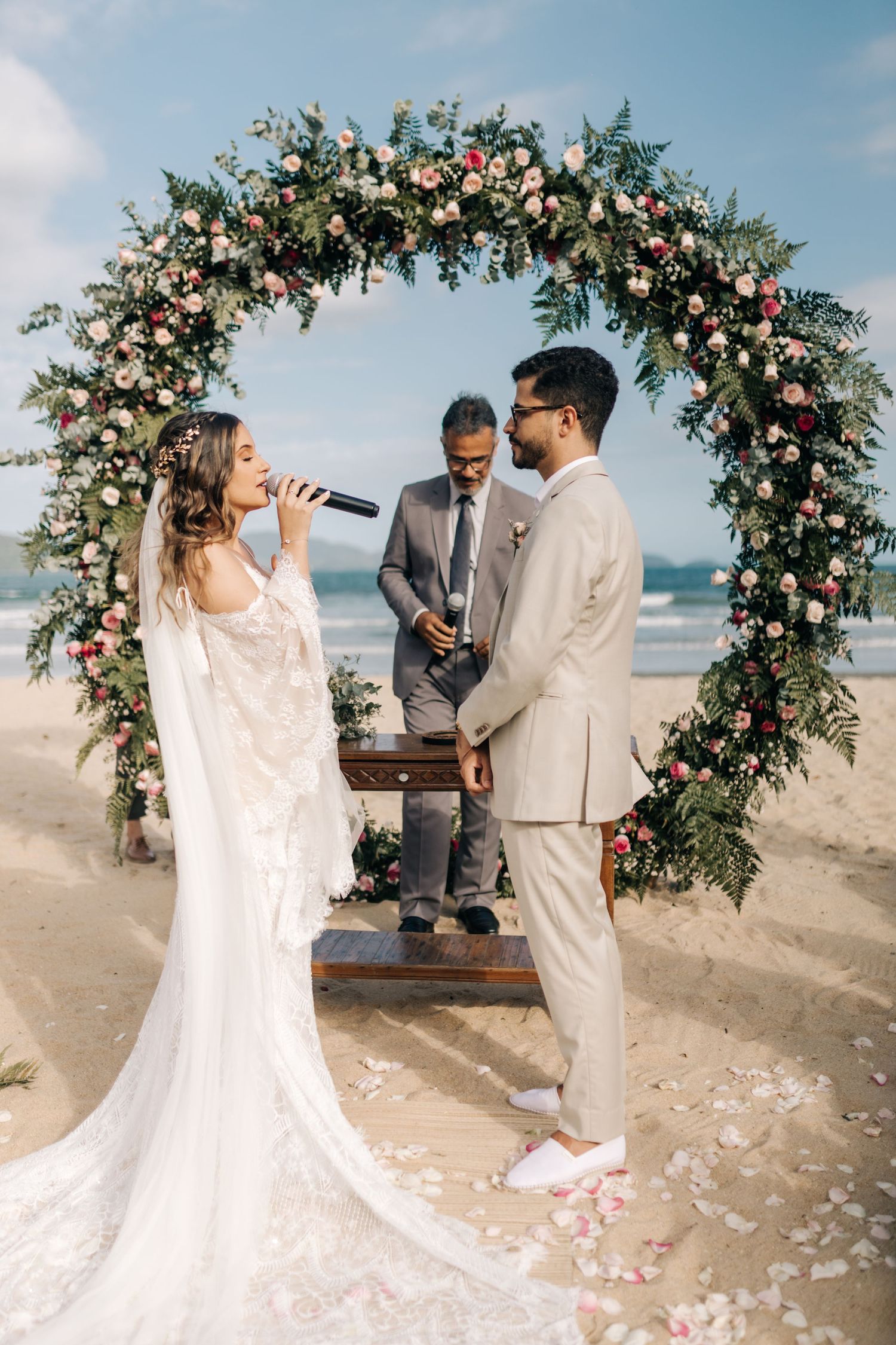 Romantic beach wedding ceremony under floral arch with ocean waves in background.