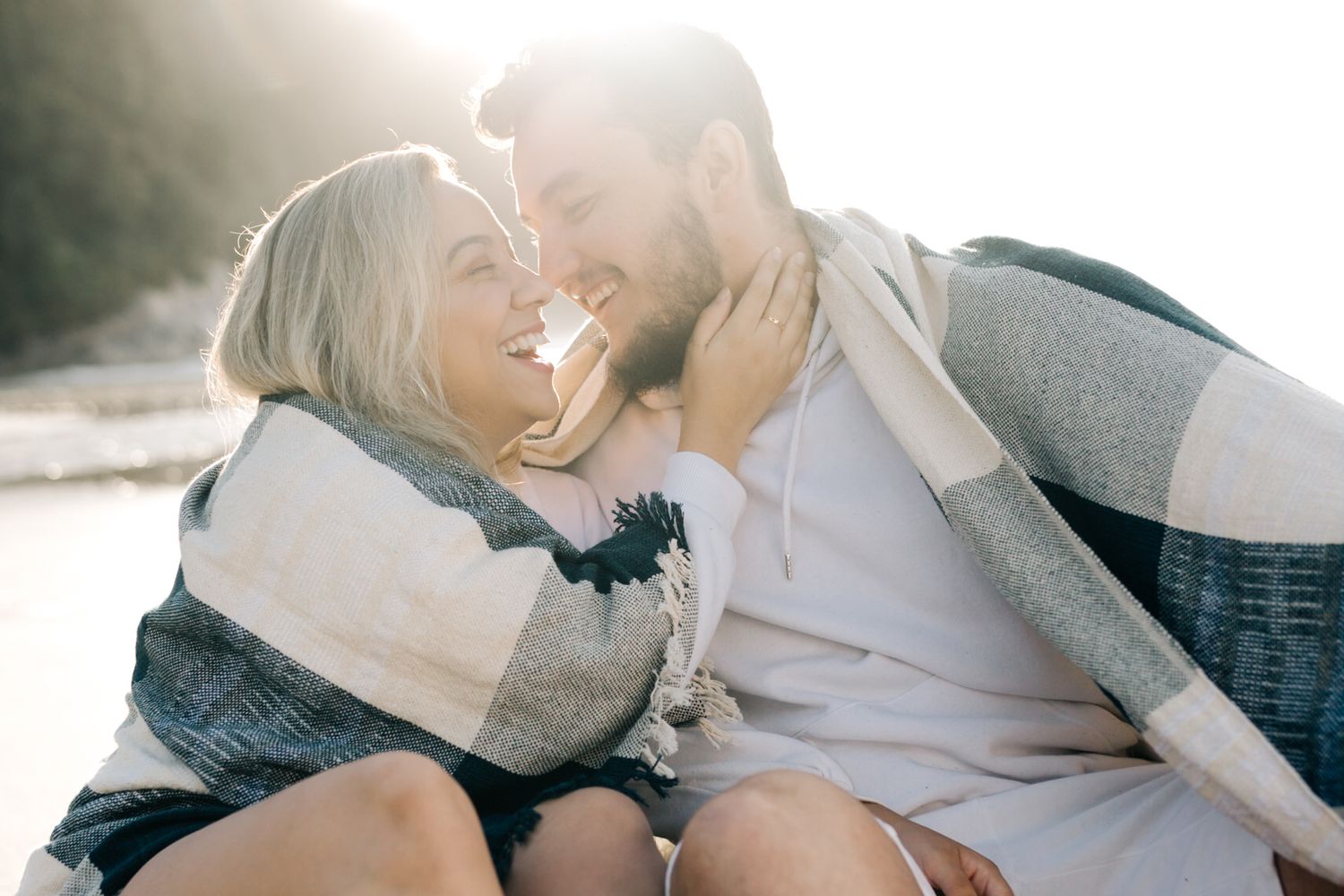 Candid beach portrait of couple laughing together wrapped in striped blanket.