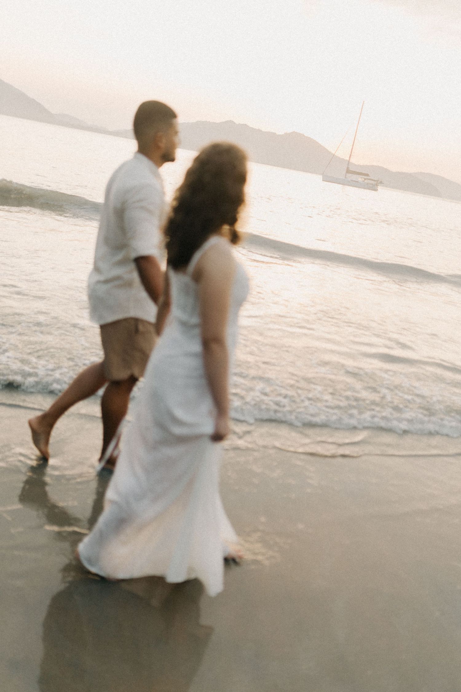 Two people dancing playfully along the shoreline at sunset.