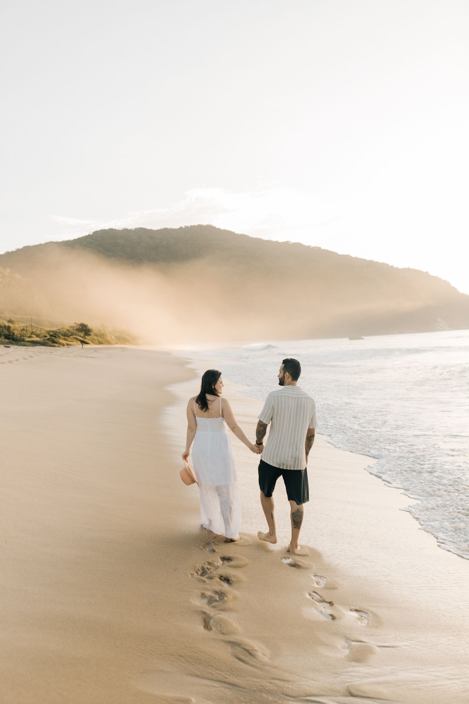 Couple walks along the sandy beach leaving footprints by the ocean waves.