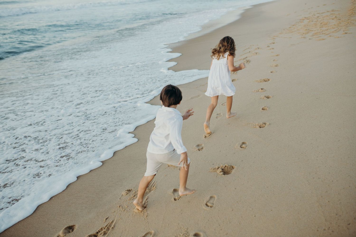 Joyful beach scene with people playing near the waves and leaving footprints in wet sand.