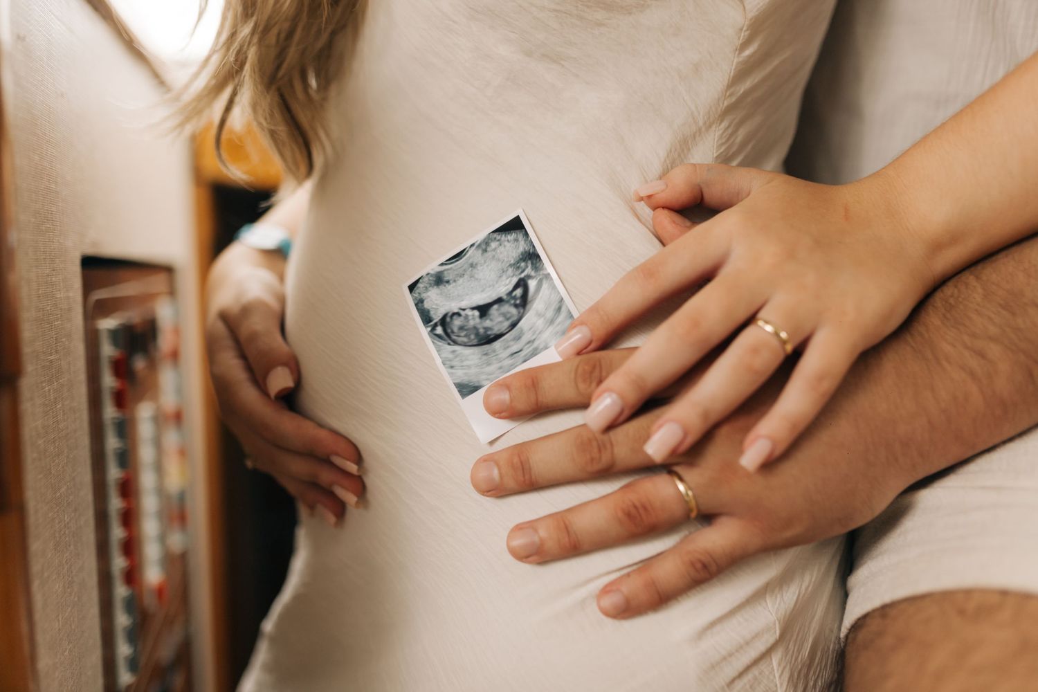 Close-up of hands holding ultrasound photo against white dress.