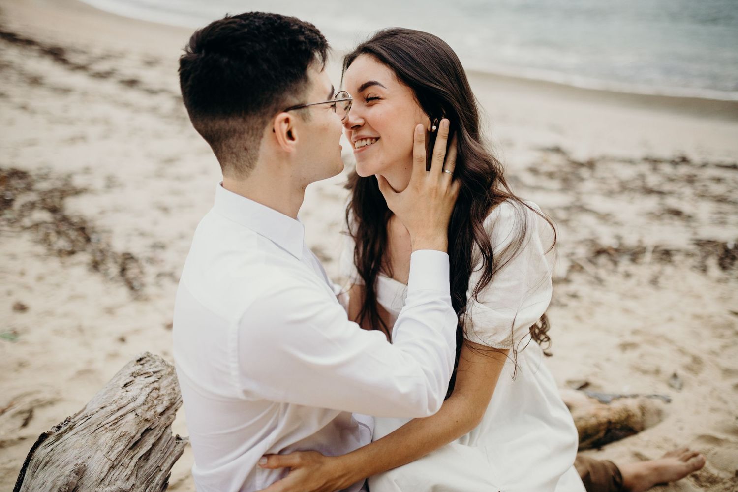Romantic couple shares intimate moments together on a beach with mountains and ocean in the background.
