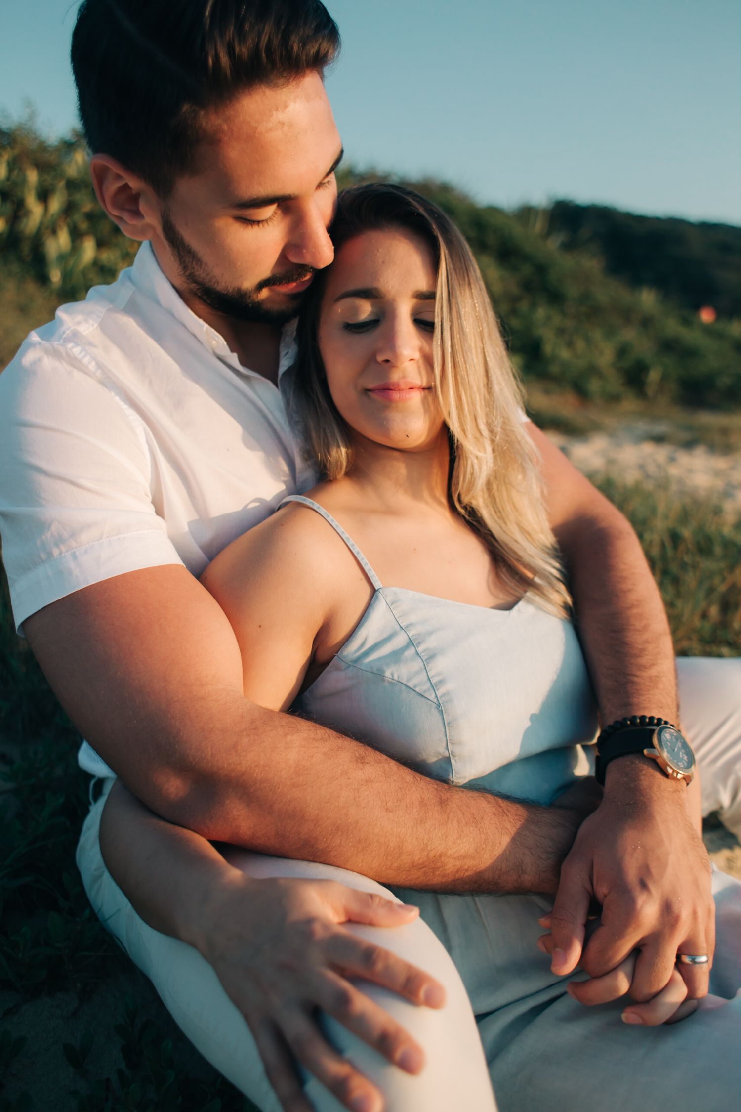 Tender moment between couple in white clothing during sunset photoshoot.