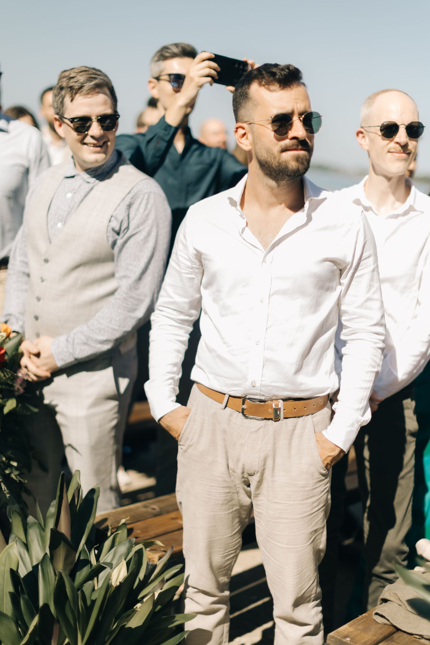 Groomsmen in light khaki pants and white shirts pose together wearing sunglasses.