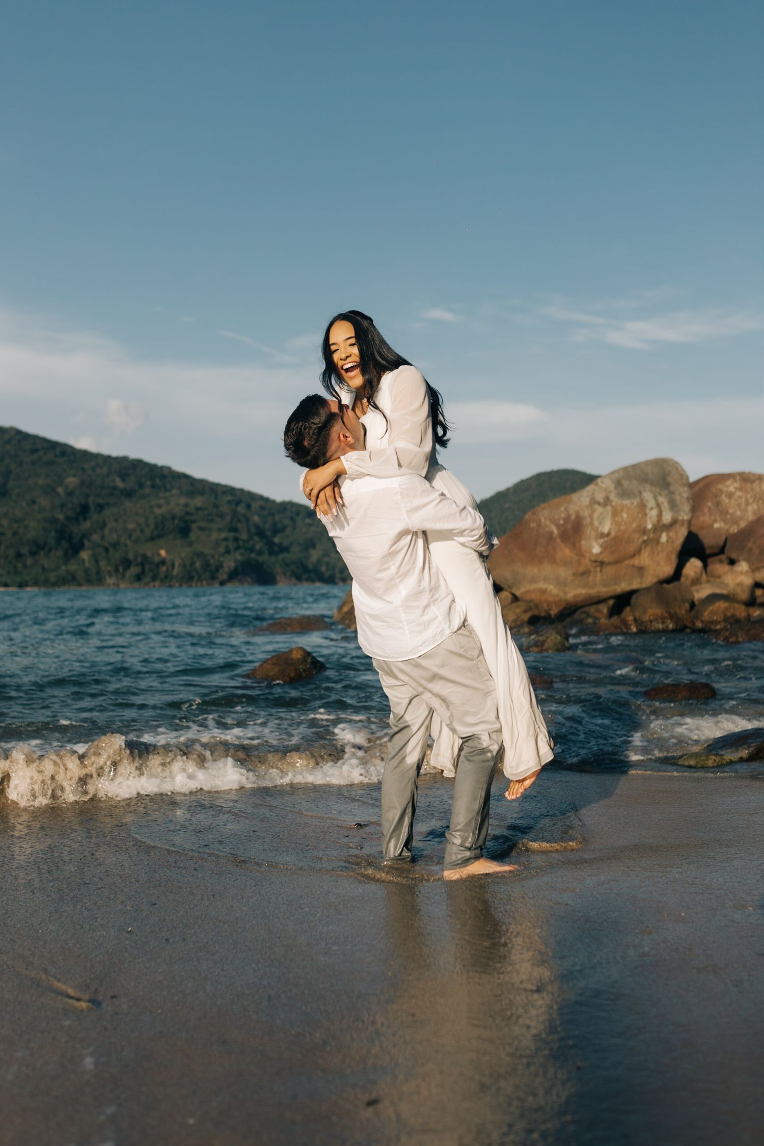 A joyful moment captured as a couple performs a lifting pose by the ocean.