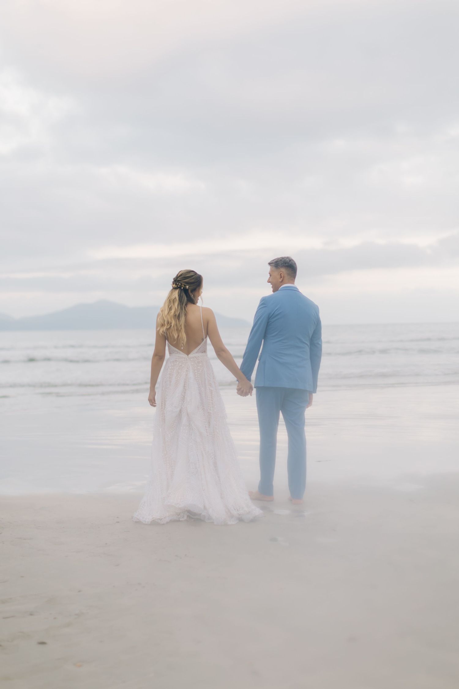 A dreamy wide shot of a couple walking along a misty beach shoreline.