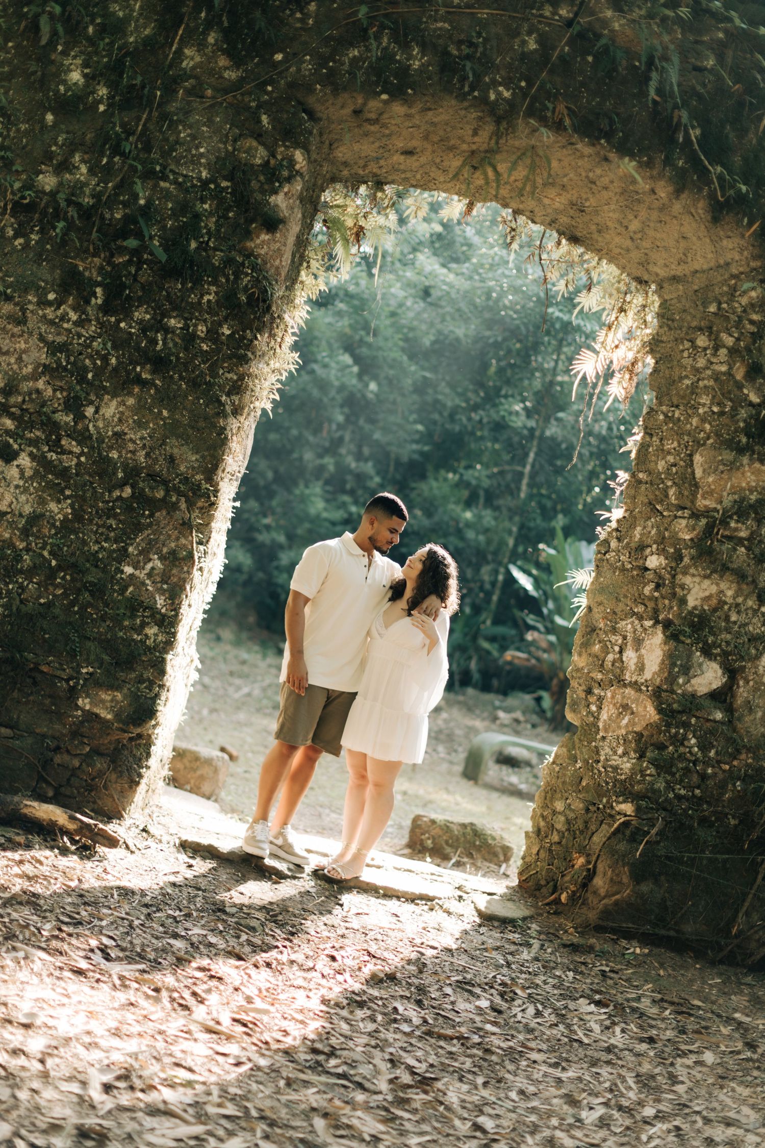 A couple standing in a stone archway surrounded by lush greenery.