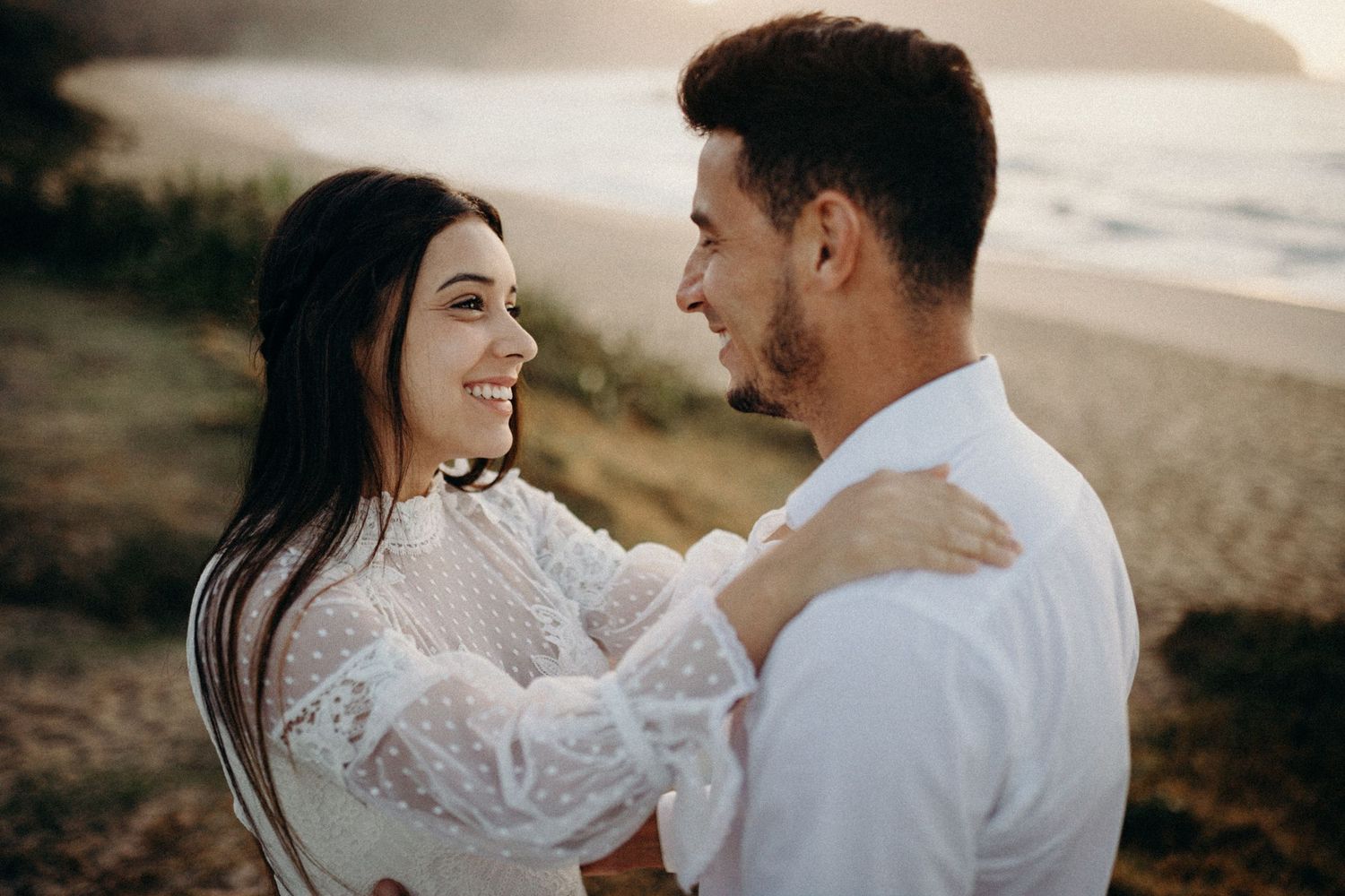 Intimate beach photo session with couple in matching white outfits.