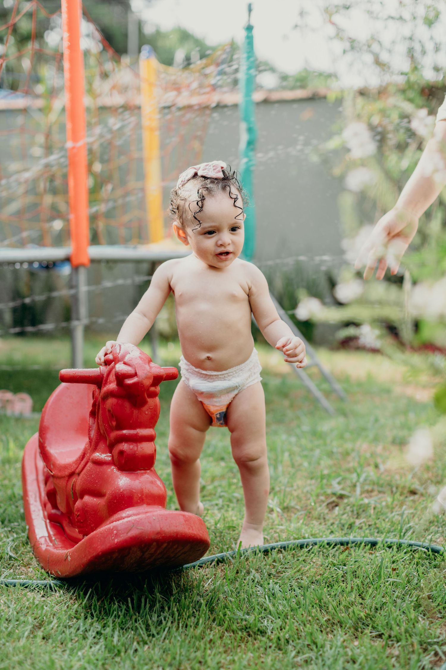 Toddler in diaper playing with red rocking toy in backyard.