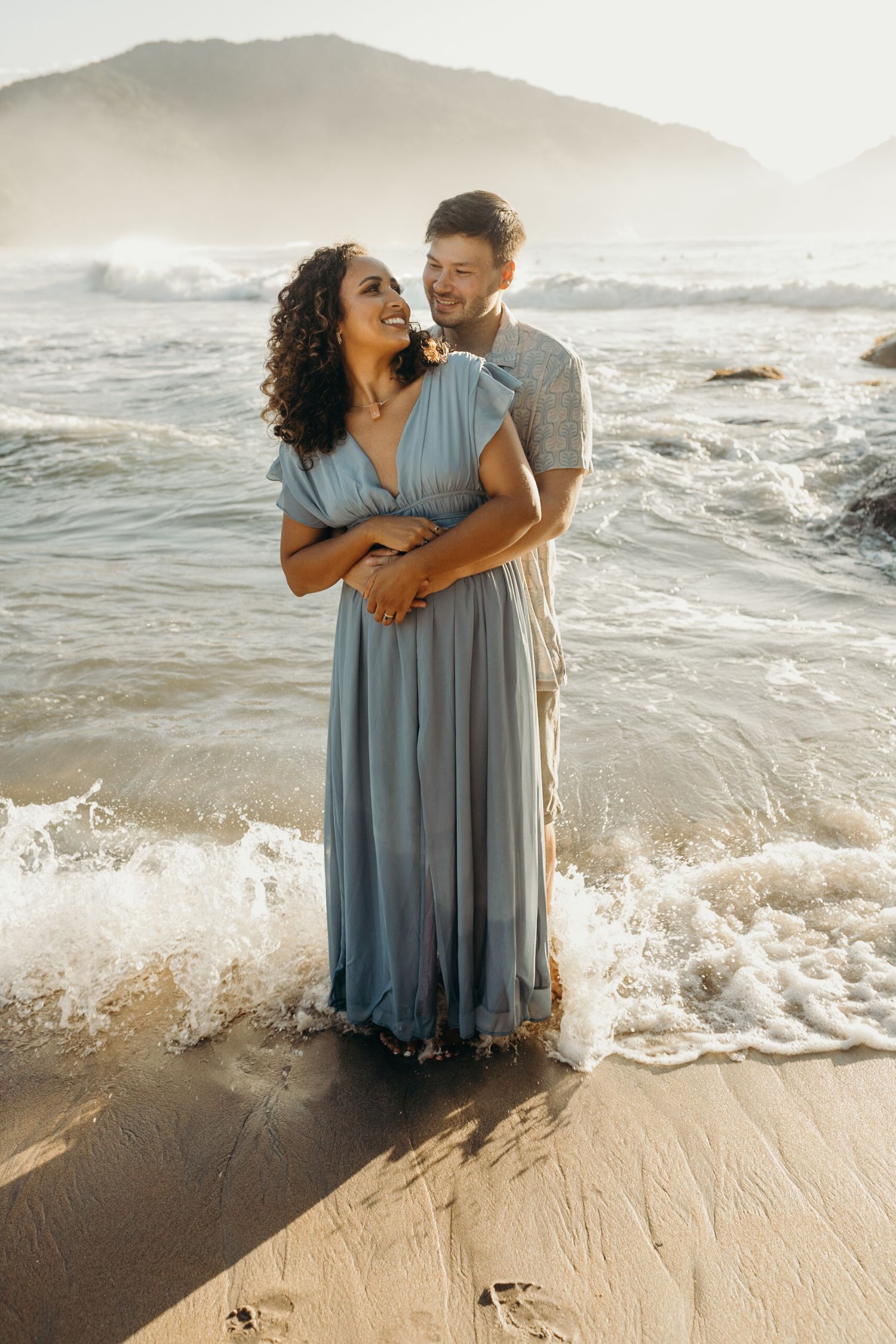 Ocean waves crash around couple during romantic beach photoshoot.