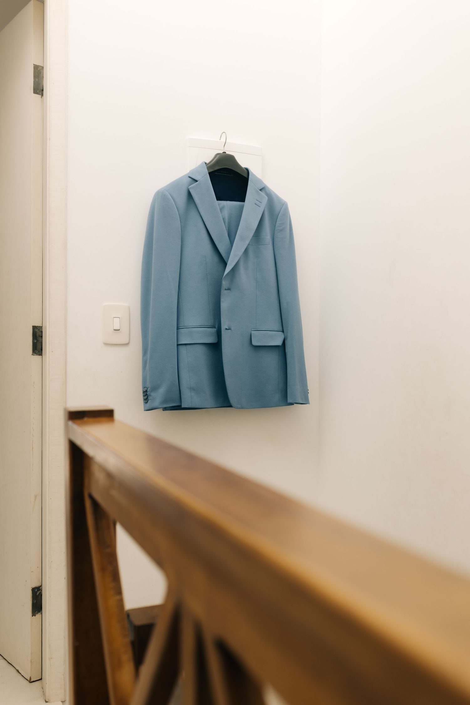 Light blue blazer displayed on hanger with wooden railing in foreground.
