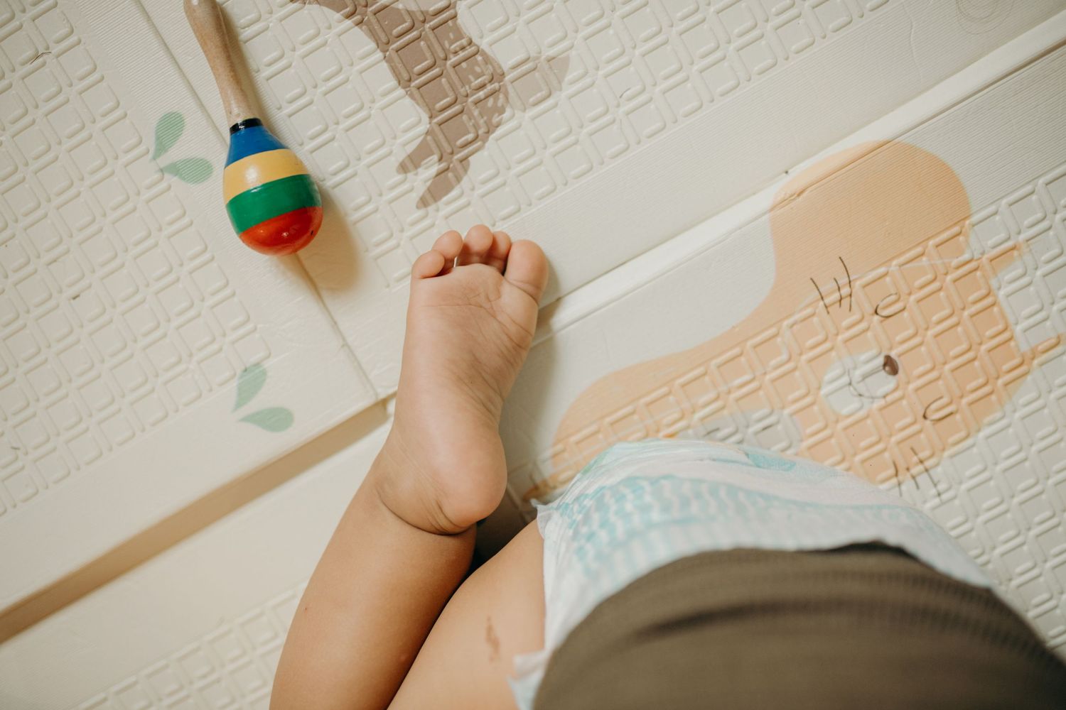 Close-up of baby foot against textured wall with toys visible.
