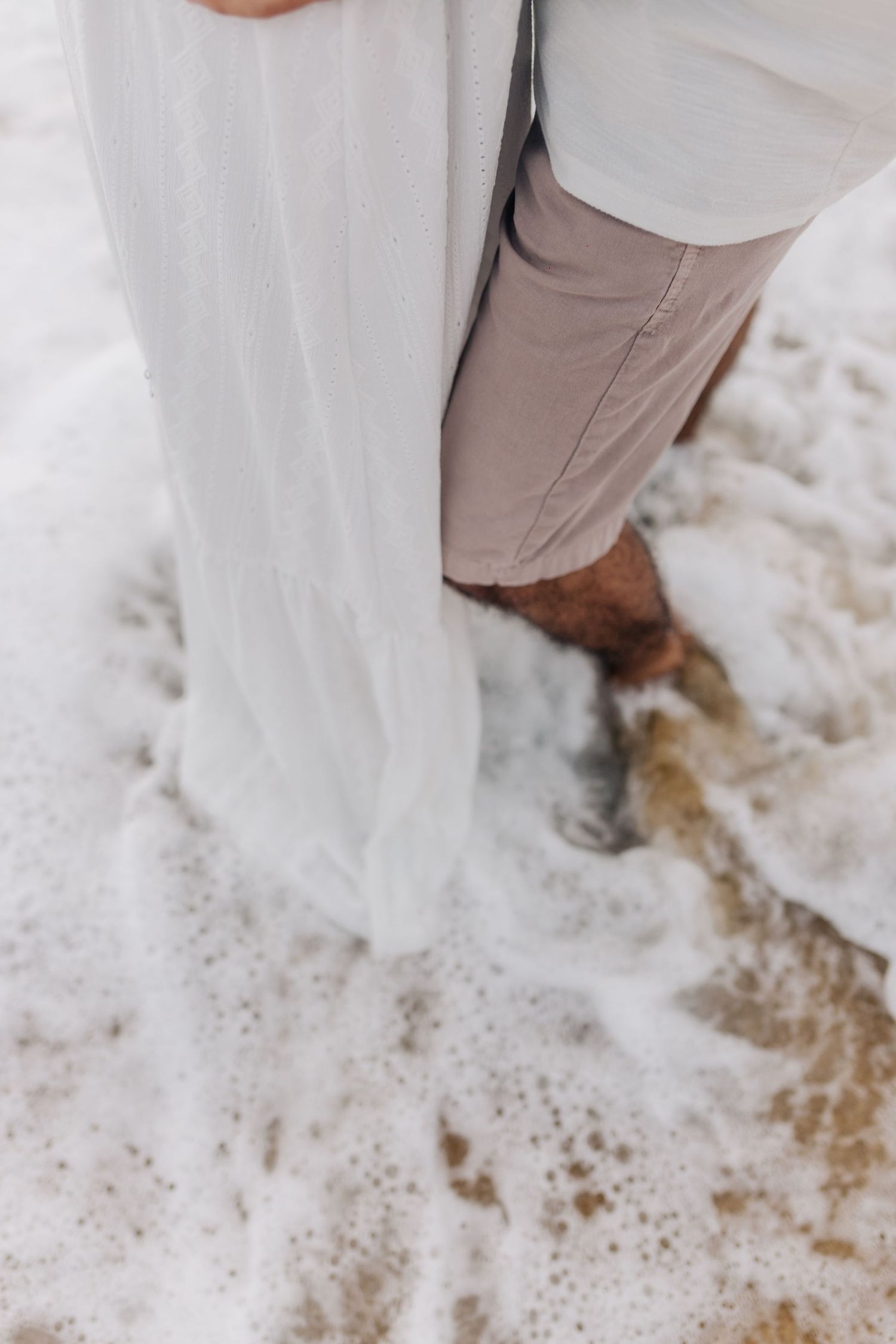 Close-up detail of white dress and khaki pants against sandy beach.