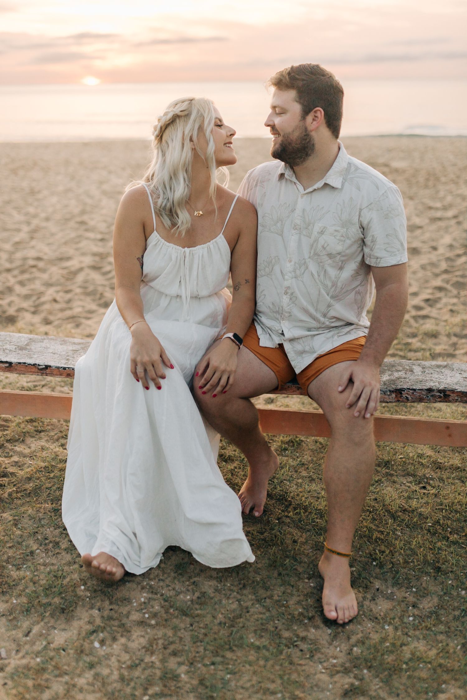 A romantic couple shares an intimate moment on a beach bench during golden hour.