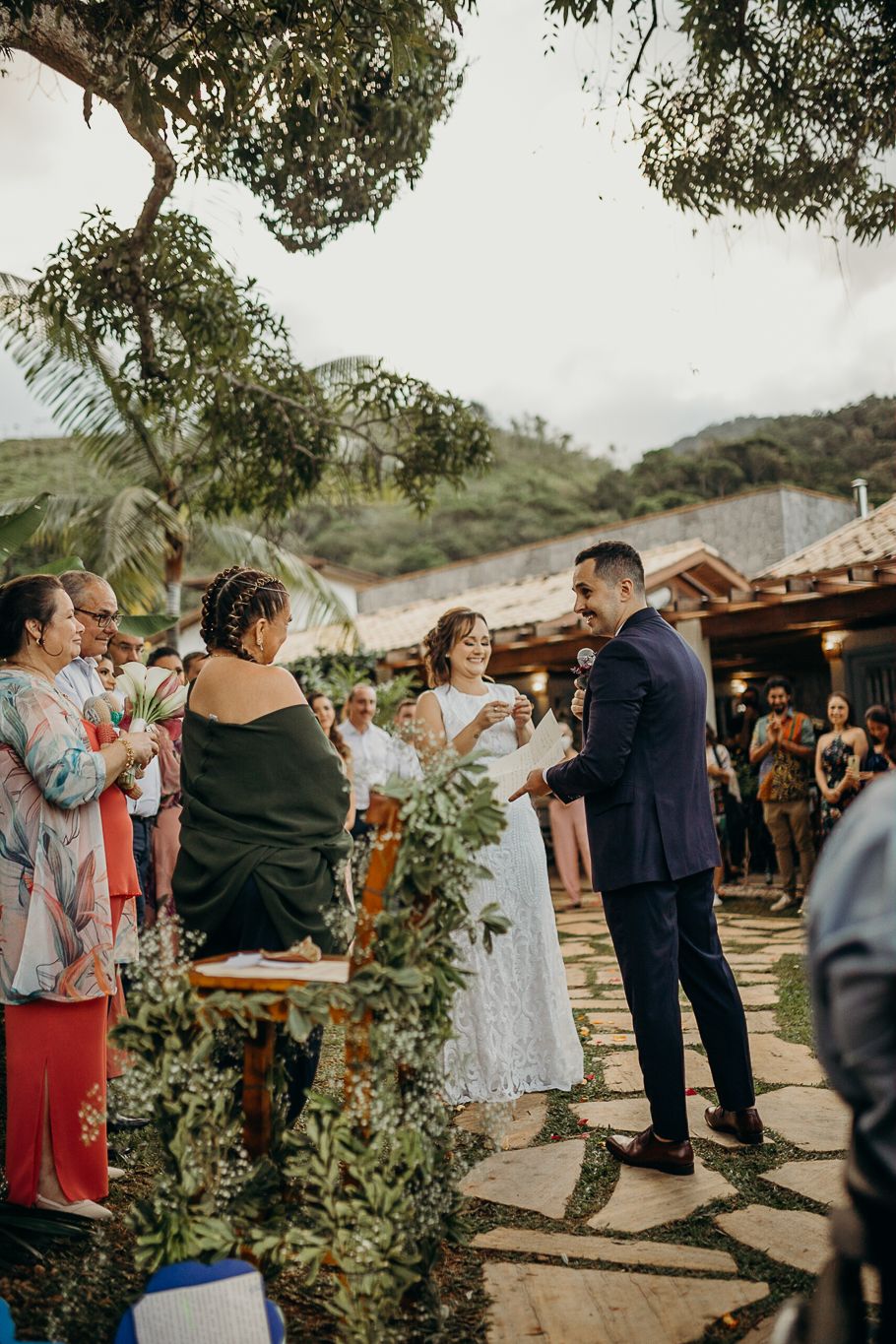 An intimate outdoor wedding ceremony with guests gathered around a stone pathway under trees.