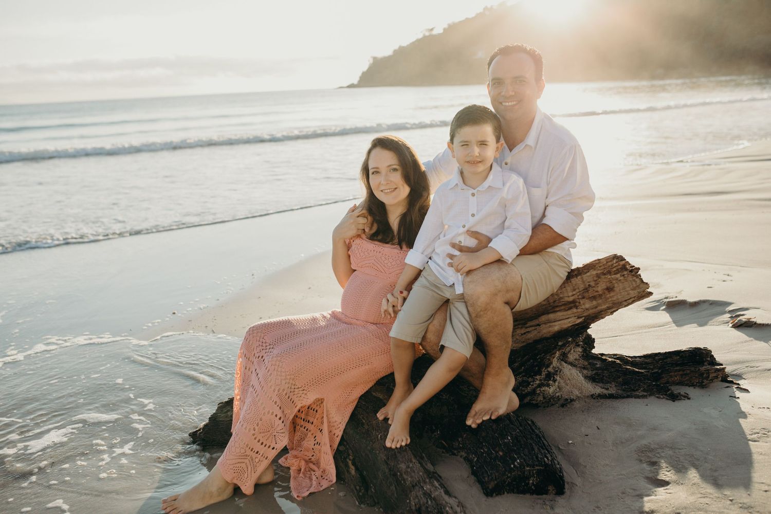 Family sitting together on rocky beach during sunset photoshoot.