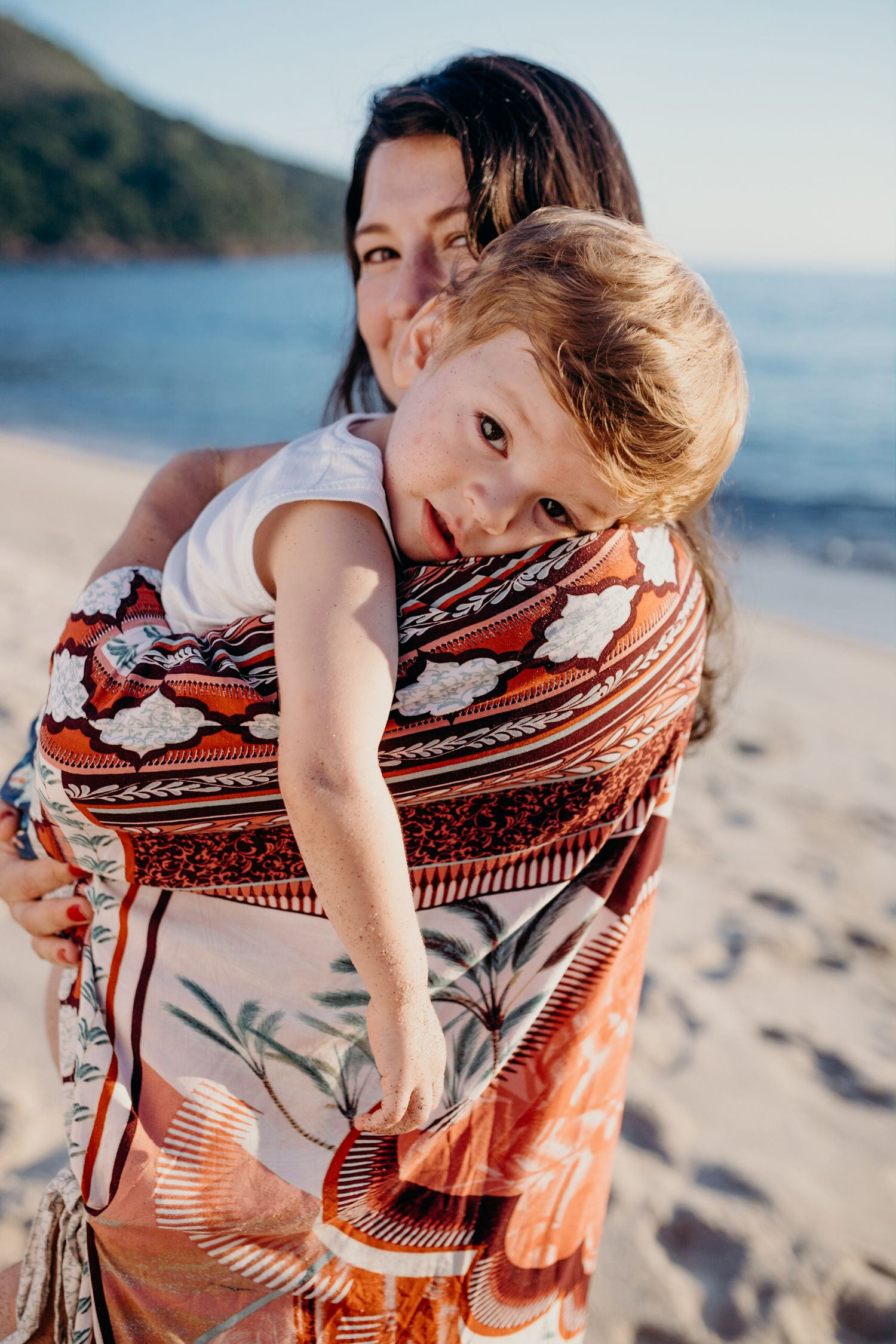 Playful moment captured on beach with orange and white patterned fabric wrap.